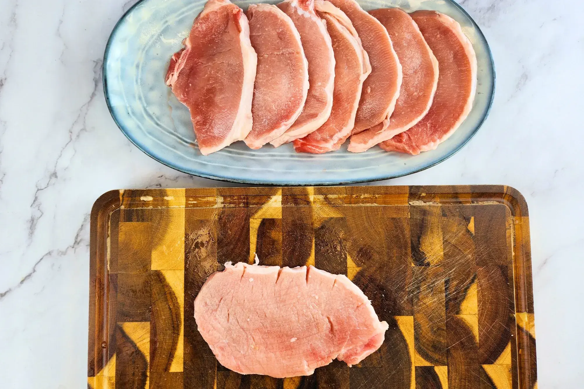 A piece of raw pork chop on the chopping board with a plate of raw pork chops