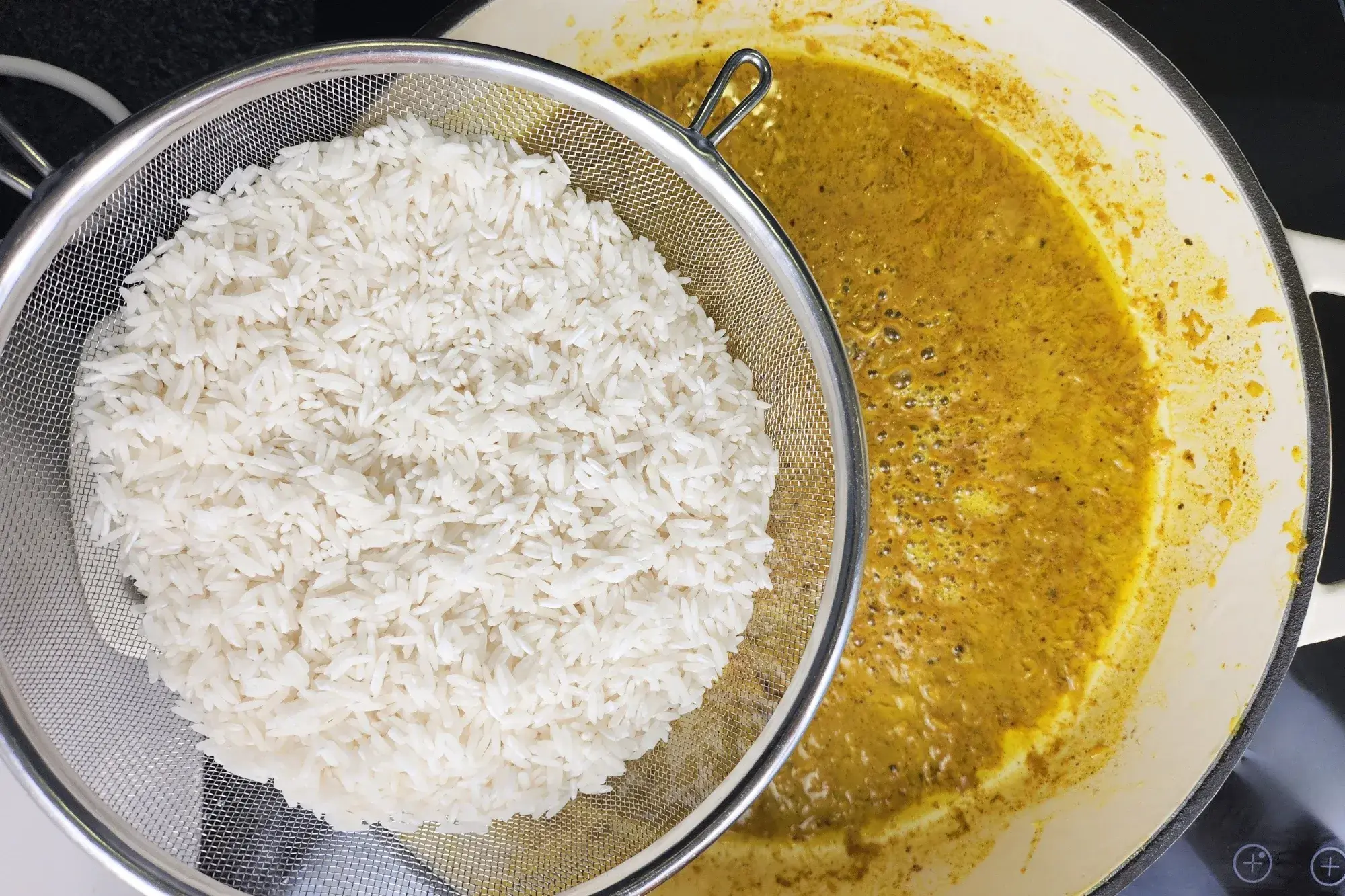 A rinsed rice is above a pan with yellow sauce.