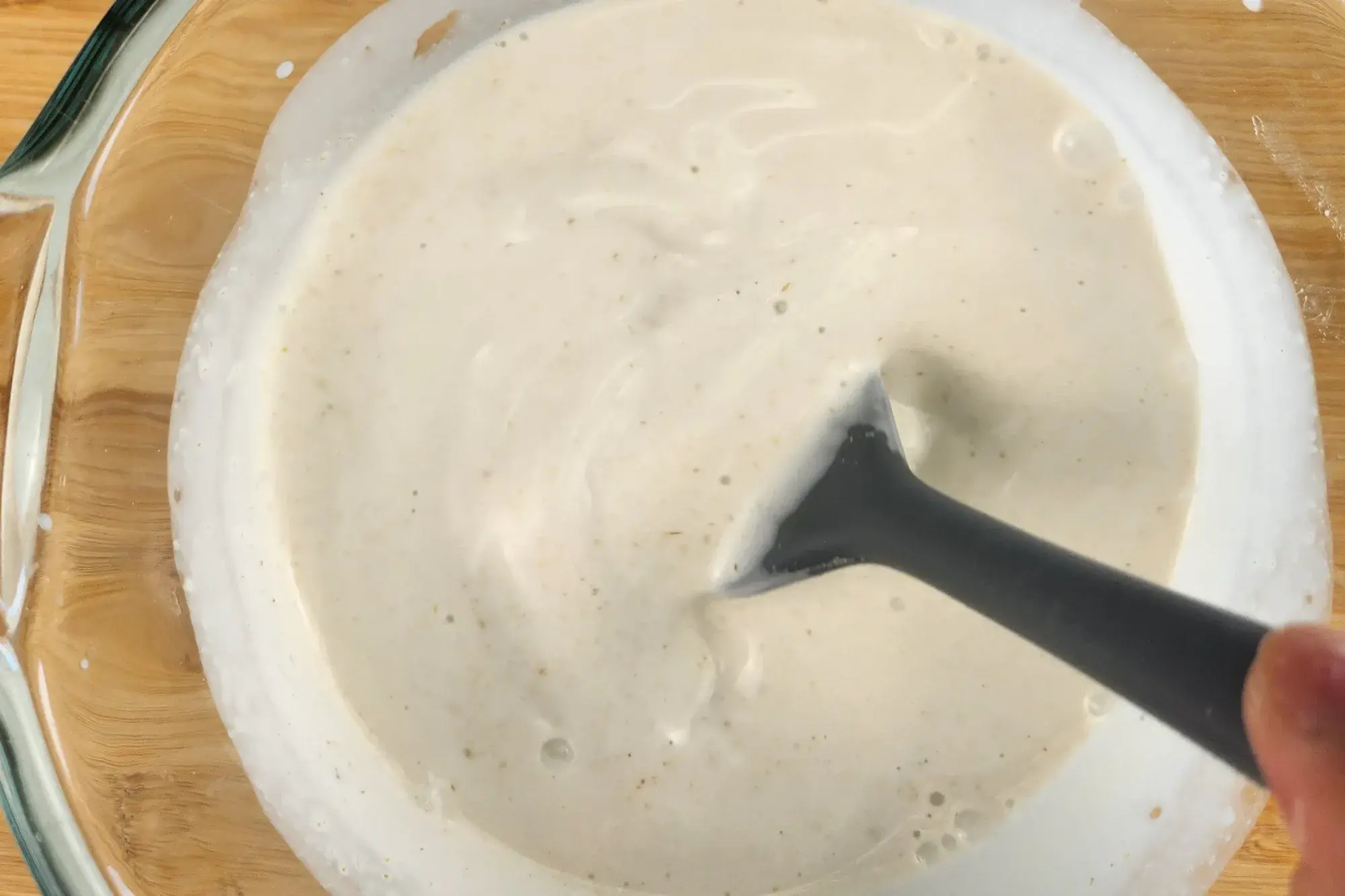 A silicone spatula is in a jar of white sauce.