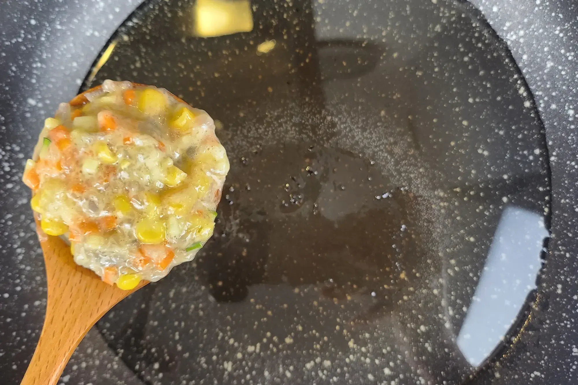 A spoon of uncooked Shrimp Fritter above a frying pan