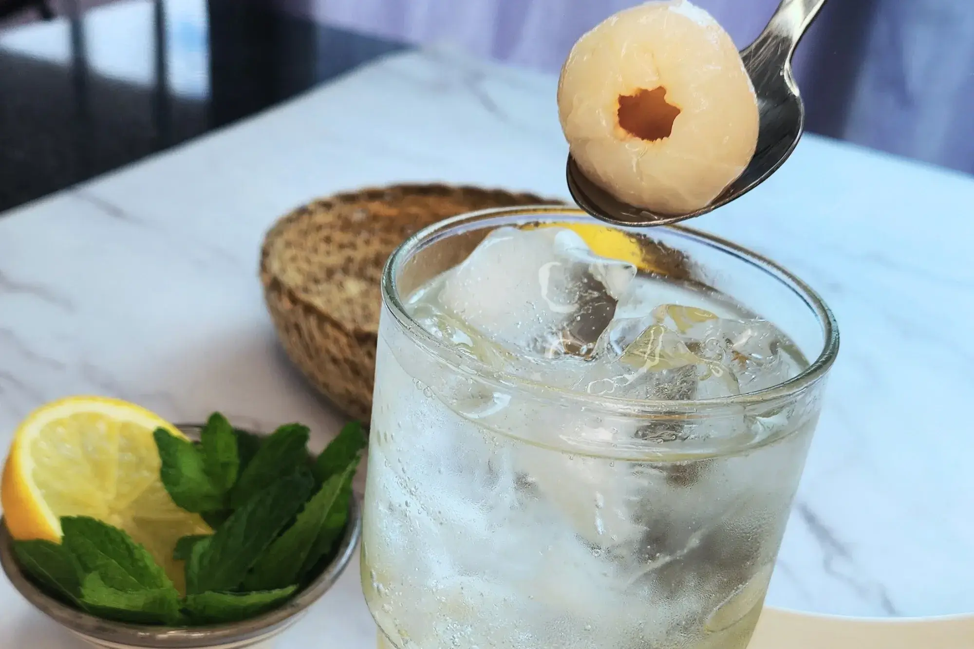 A spoon with lychee is being held above a glass full of liquid.