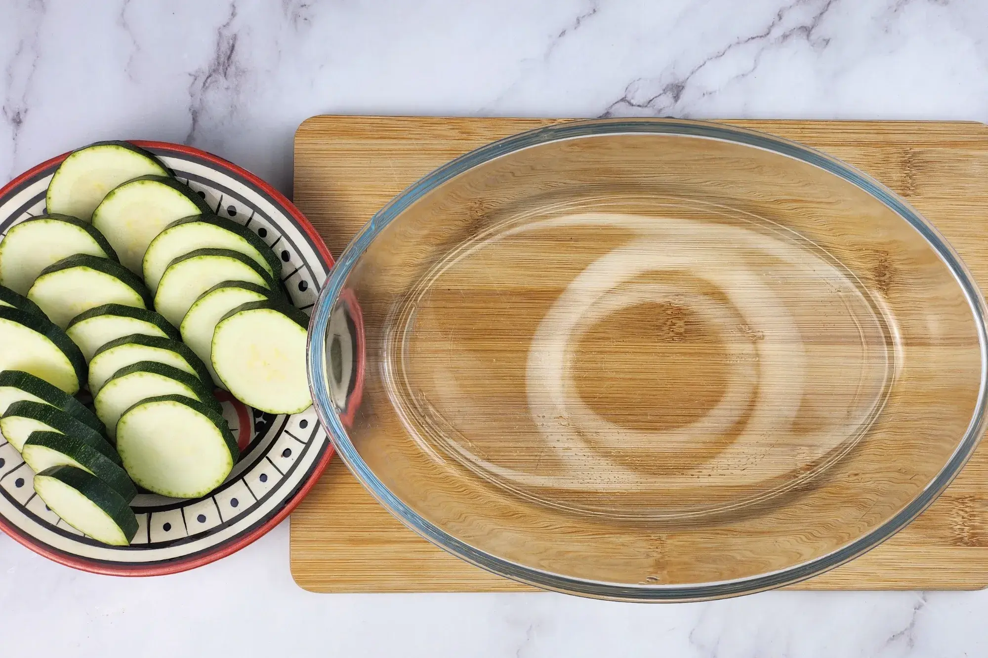 An empty baking bowl is next to a plate of sliced zucchini