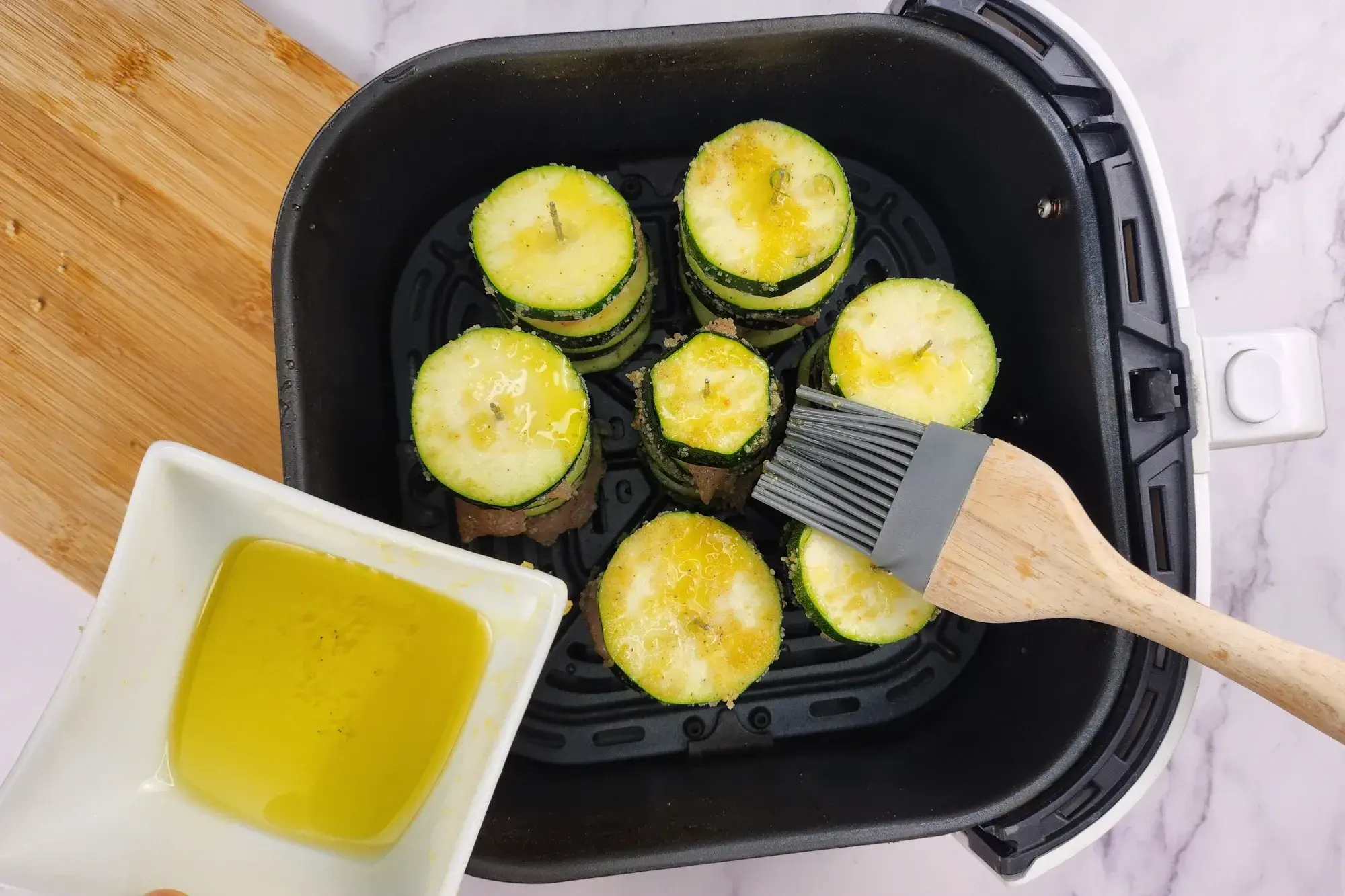 Chicken and Zucchini Skewers in a air fryer basket with brushing olive oil.