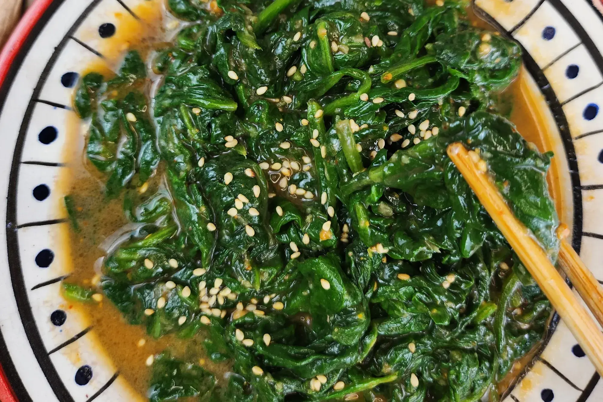 Chopsticks are holding spinach salad