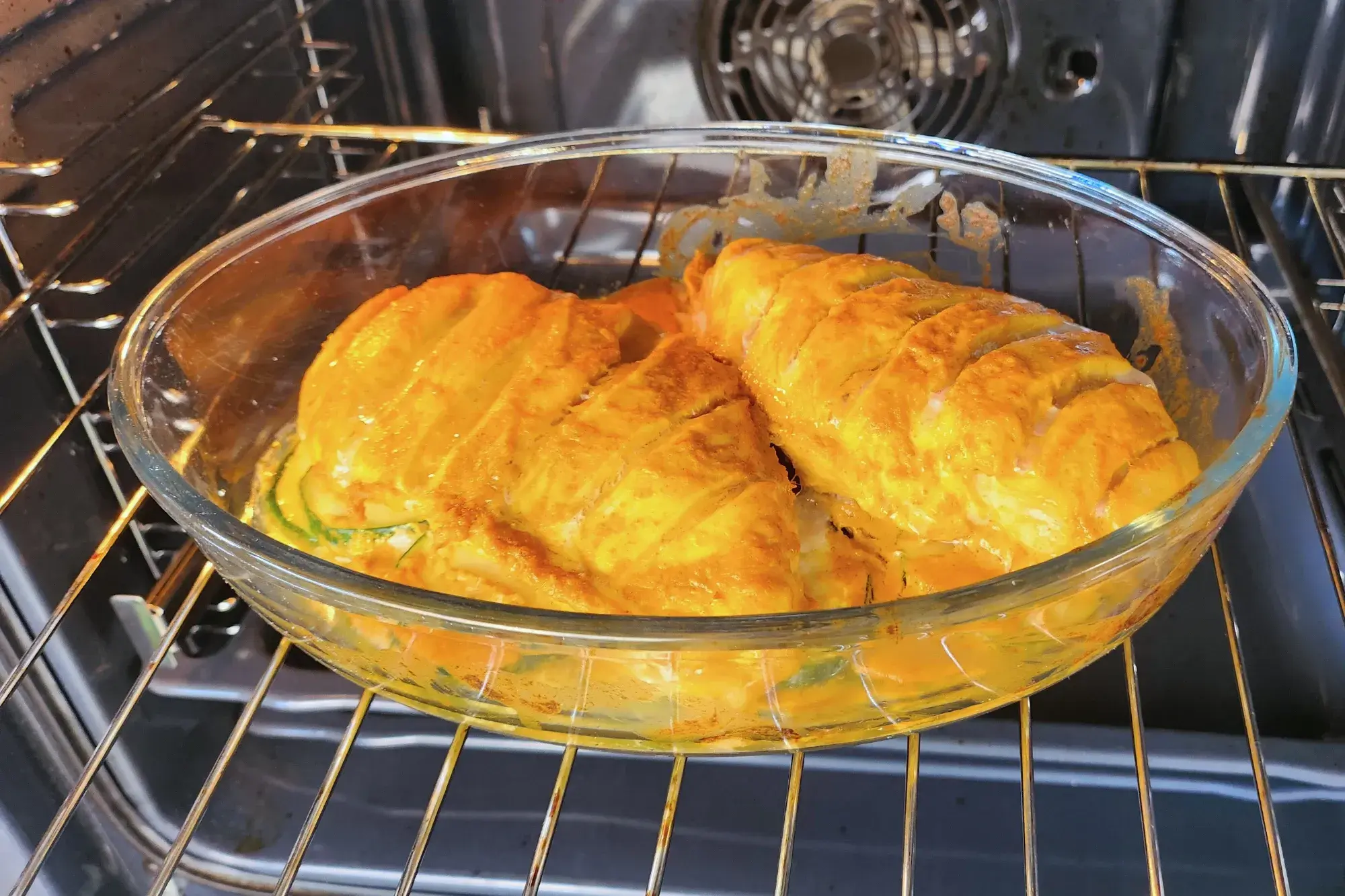 Two marinated chicken breasts are in a baking bowl in an oven
