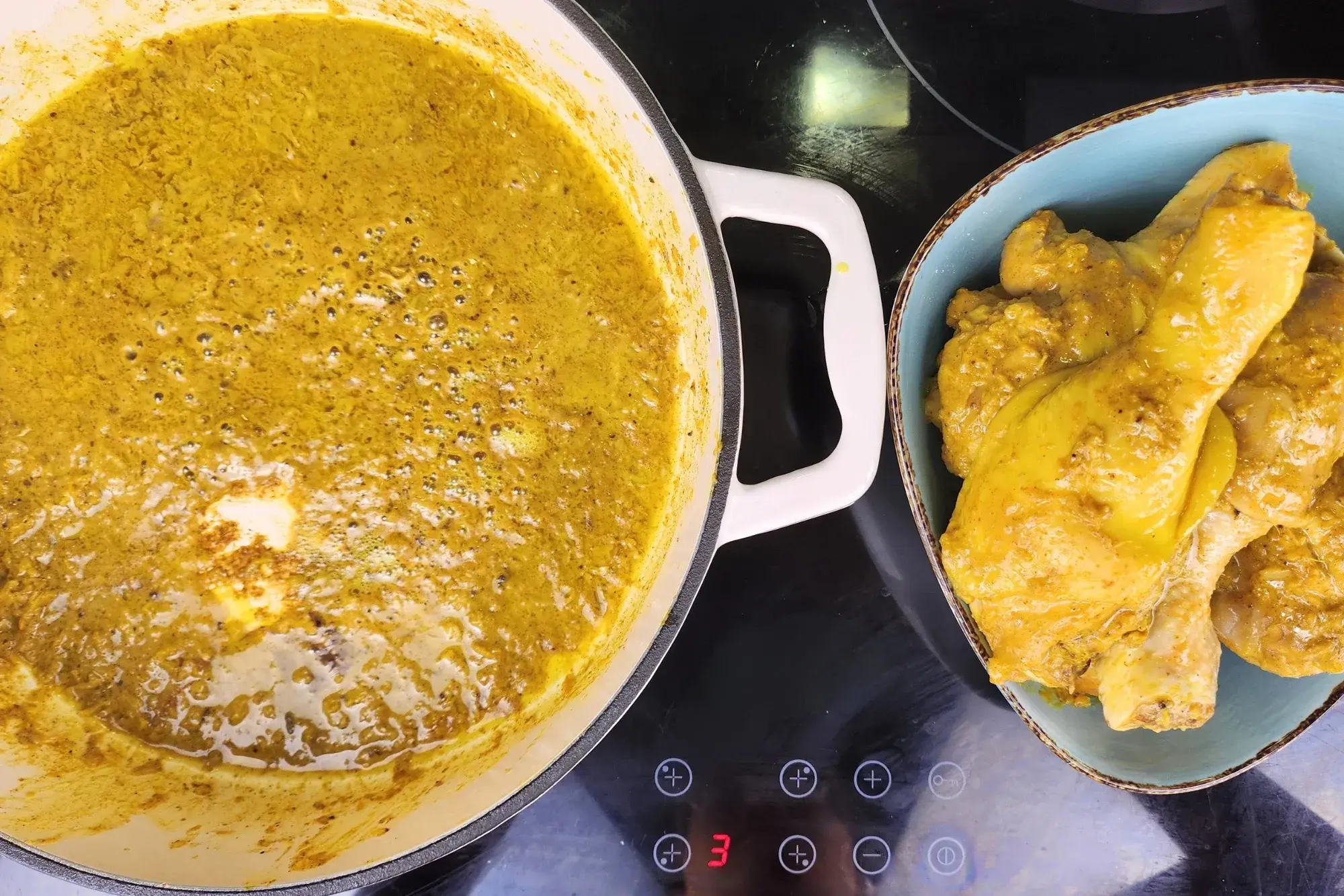 Cooked chicken in a bowl is next to a pan with yellow sauce.