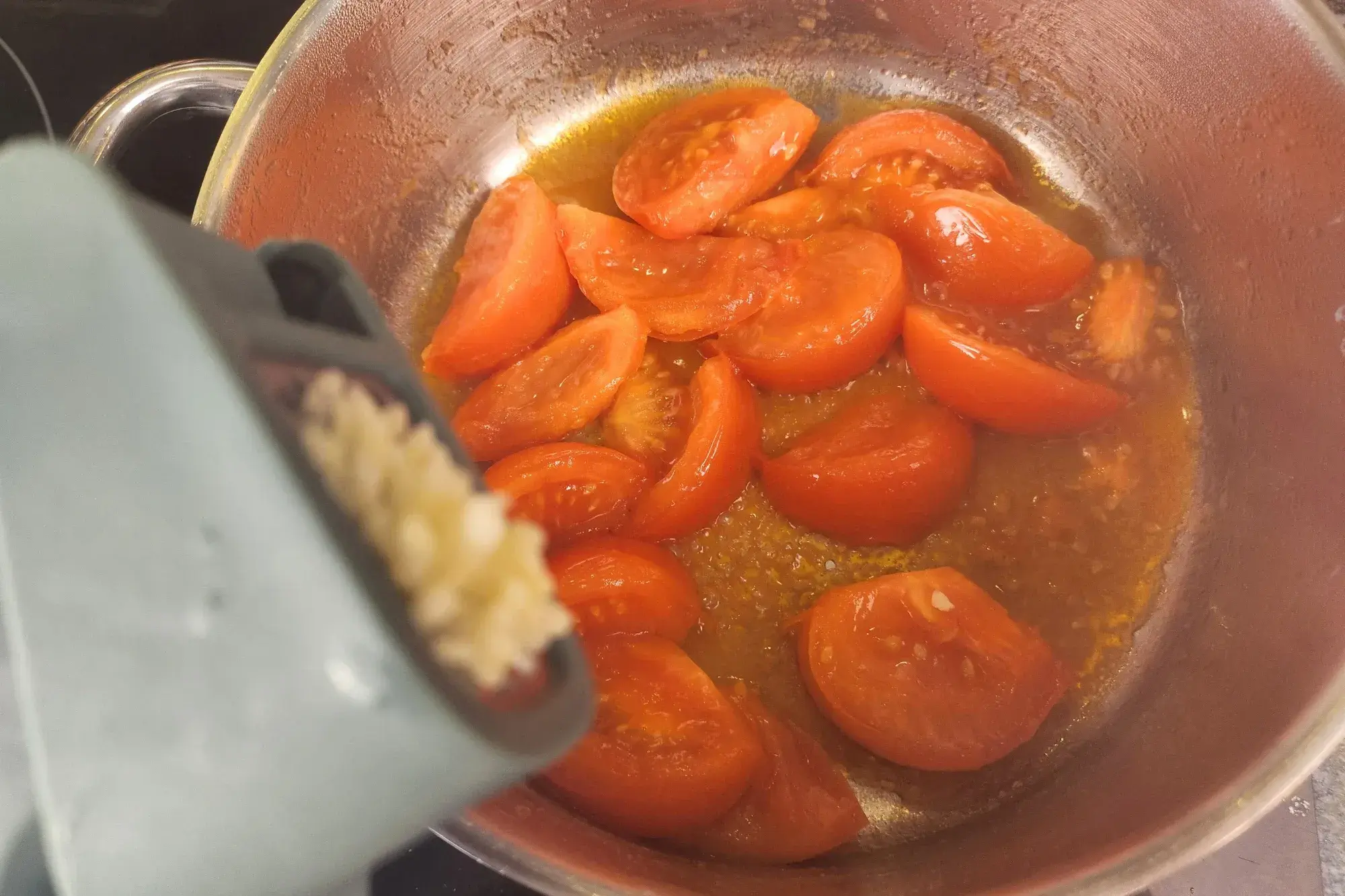 Minced garlic is above a pot of cooked tomatoes.