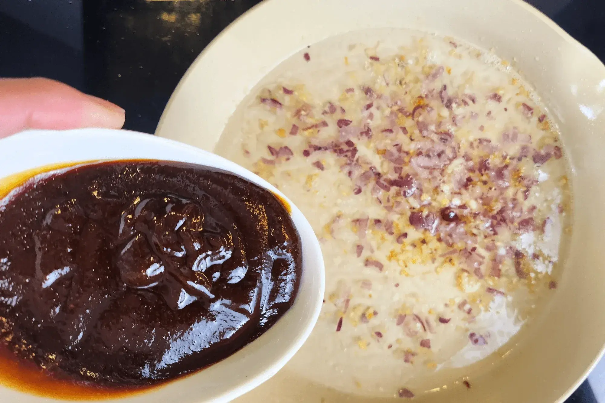 a hand holding a bowl of hoisin sauce with the sauce pan