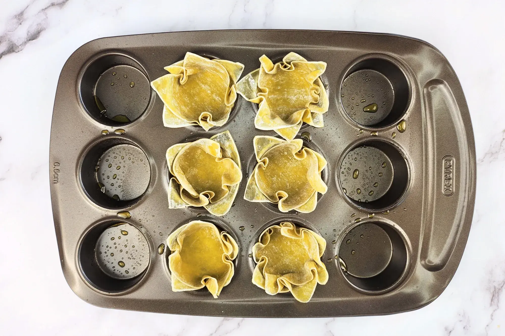 Six wonton cups in a muffin tray.