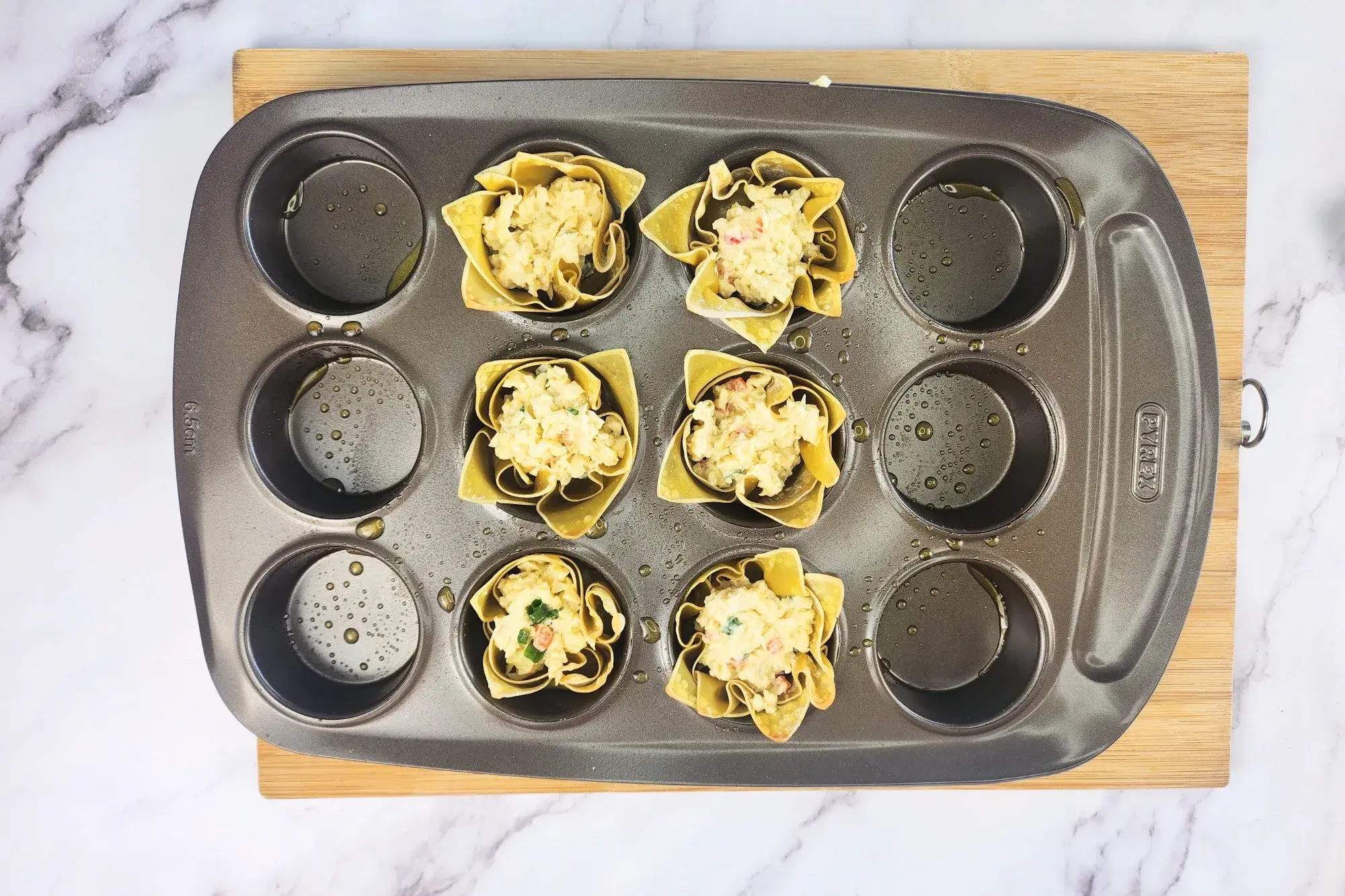 Six wonton cups with filling in a muffin tray.