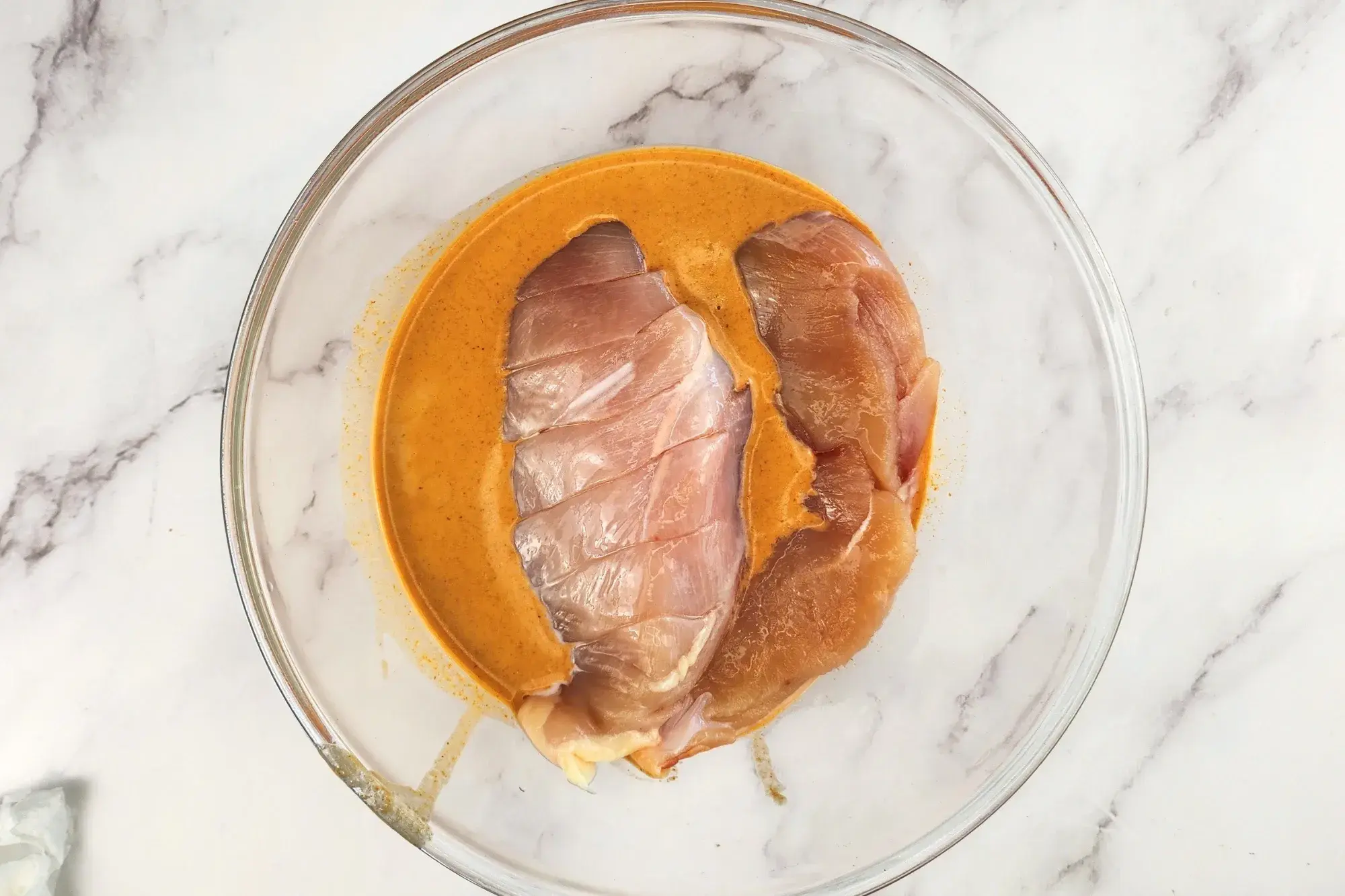 Two chicken breasts are in a mixing bowl with marinating sauce
