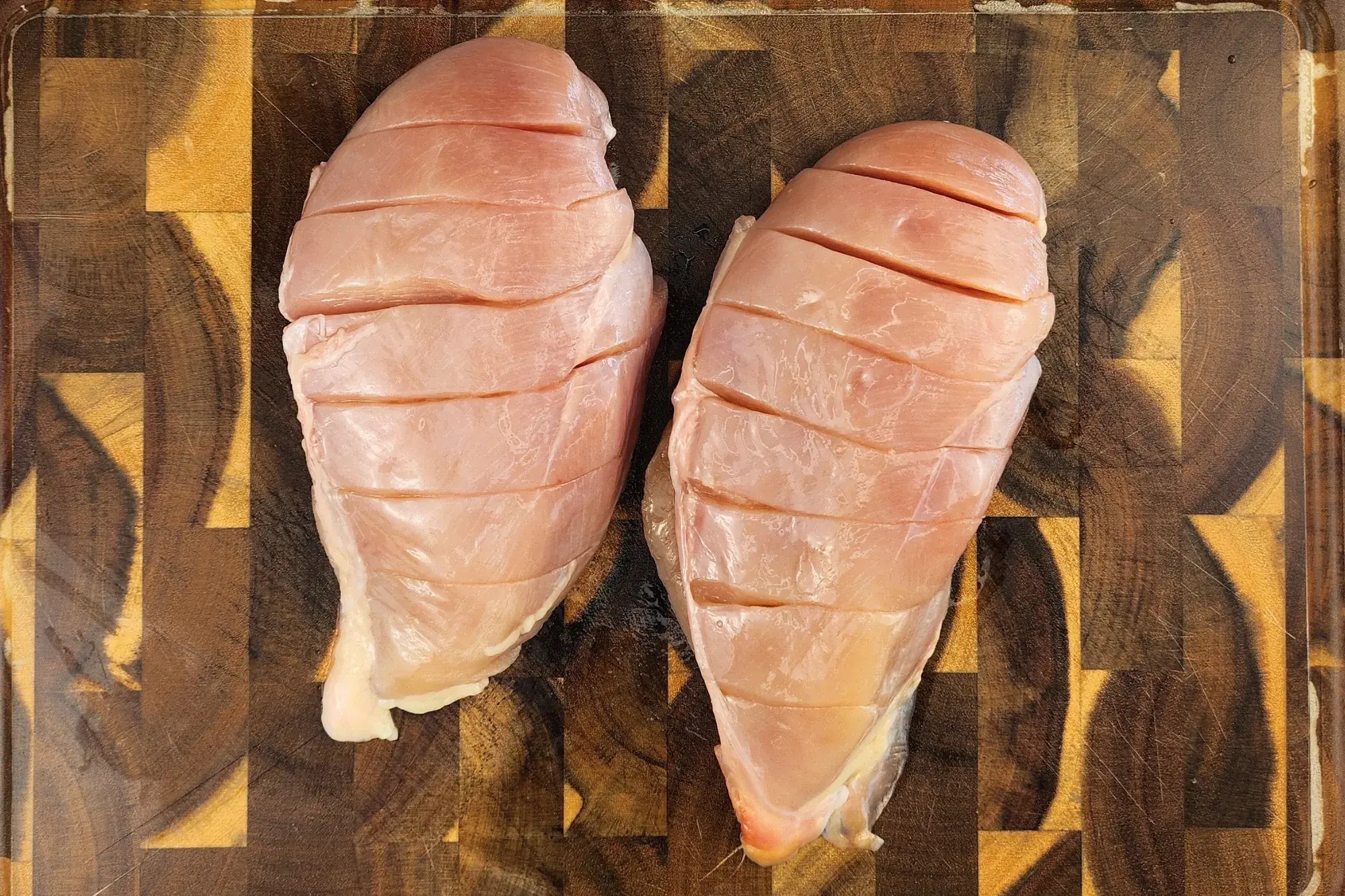 Two cut chicken breasts are on chopping board