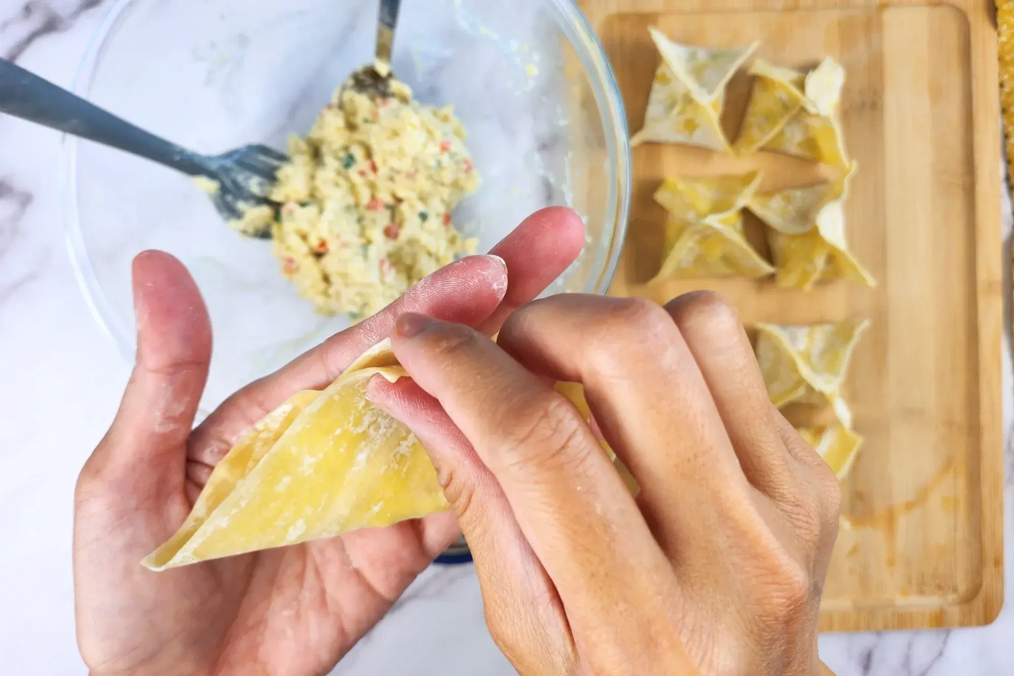 Two hands are folding the wonton into triangle shape.