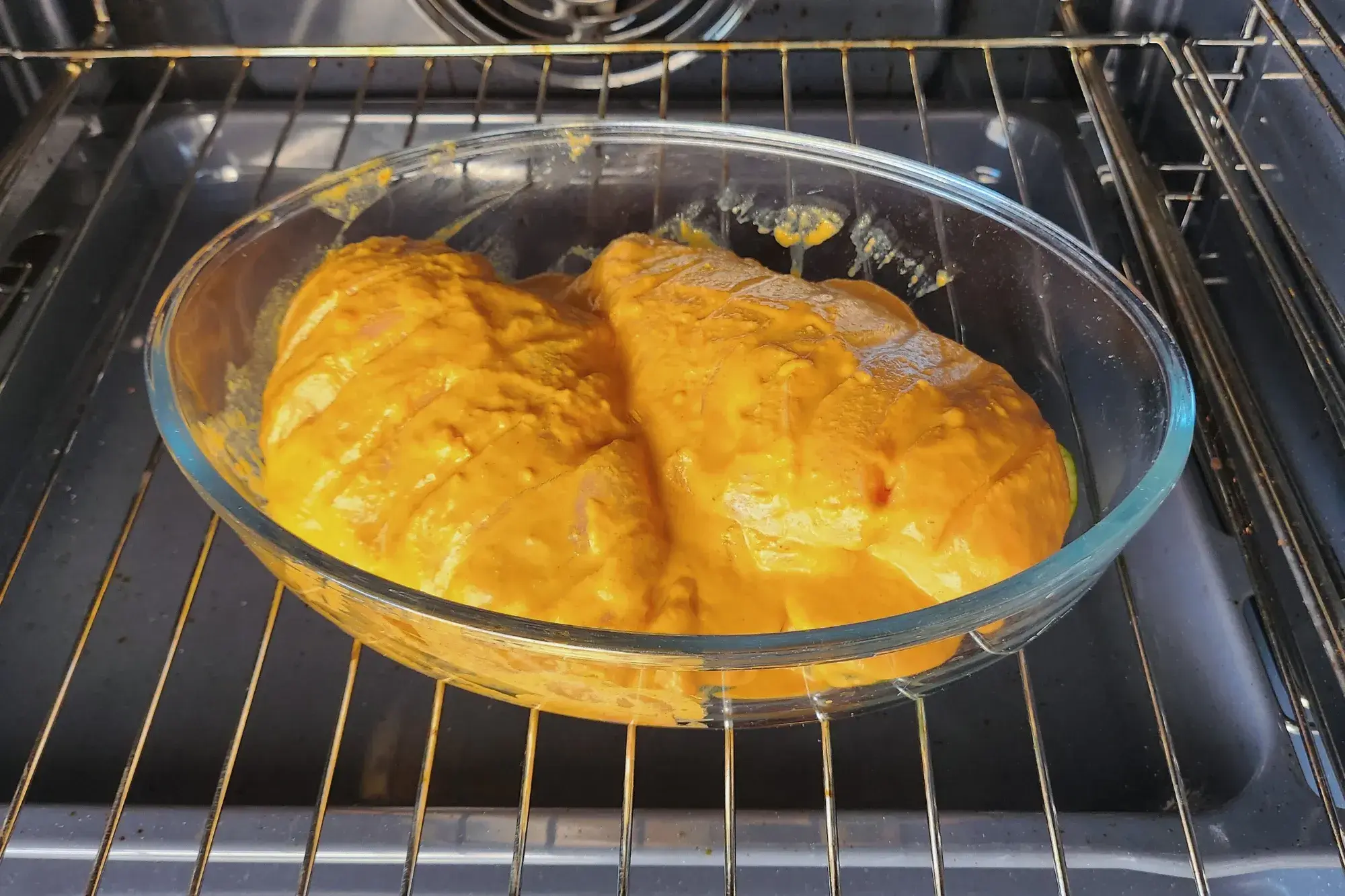 Two marinated chicken breasts are in a baking bowl in an oven