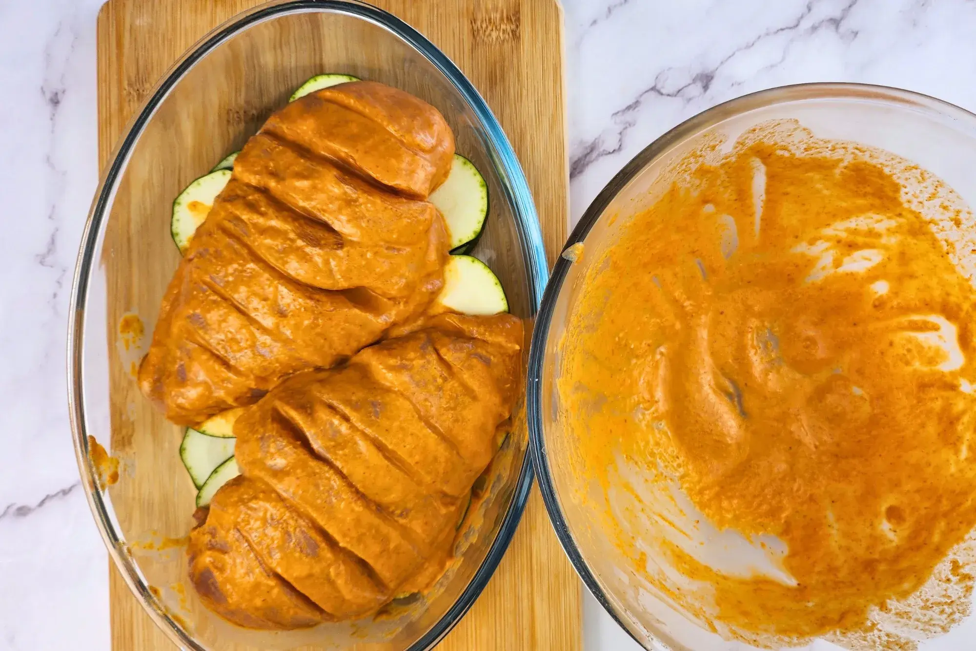 Two marinated chicken breasts are in a baking bowl is next to a mixing bowl