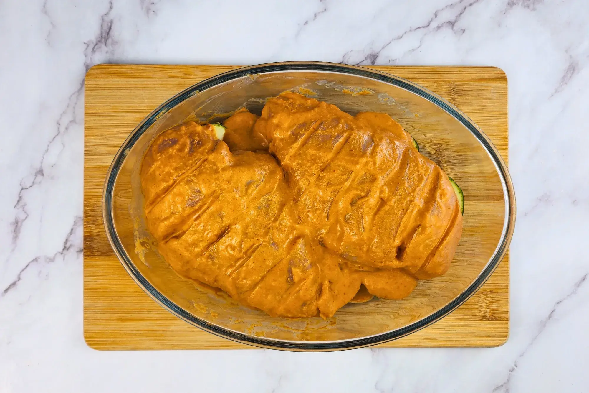 Two marinated chicken breasts are in a baking bowl is next to a mixing bowl