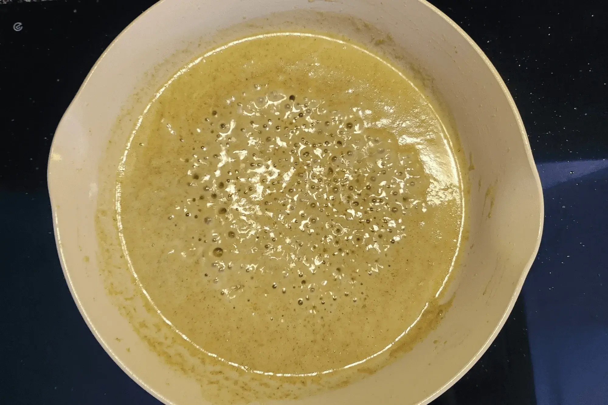 In the first pan, heat a portion of the coconut milk over medium heat until it begins to simmer. Add the green curry paste and stir well until it's fragrant. You will see the green oil showing on the surface.