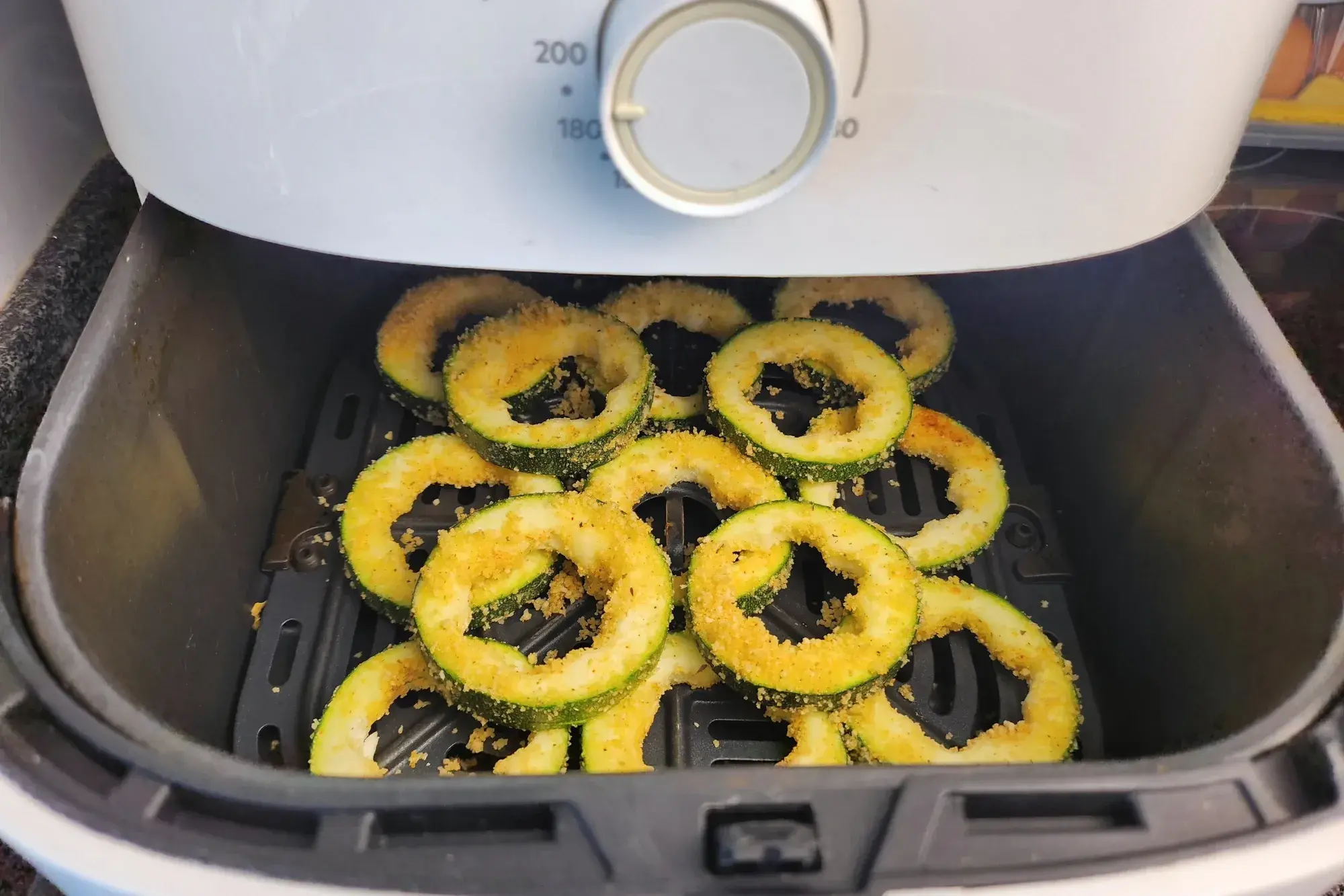 Zucchini rings in mixing bowl and Zucchini rings in basket of air fryer