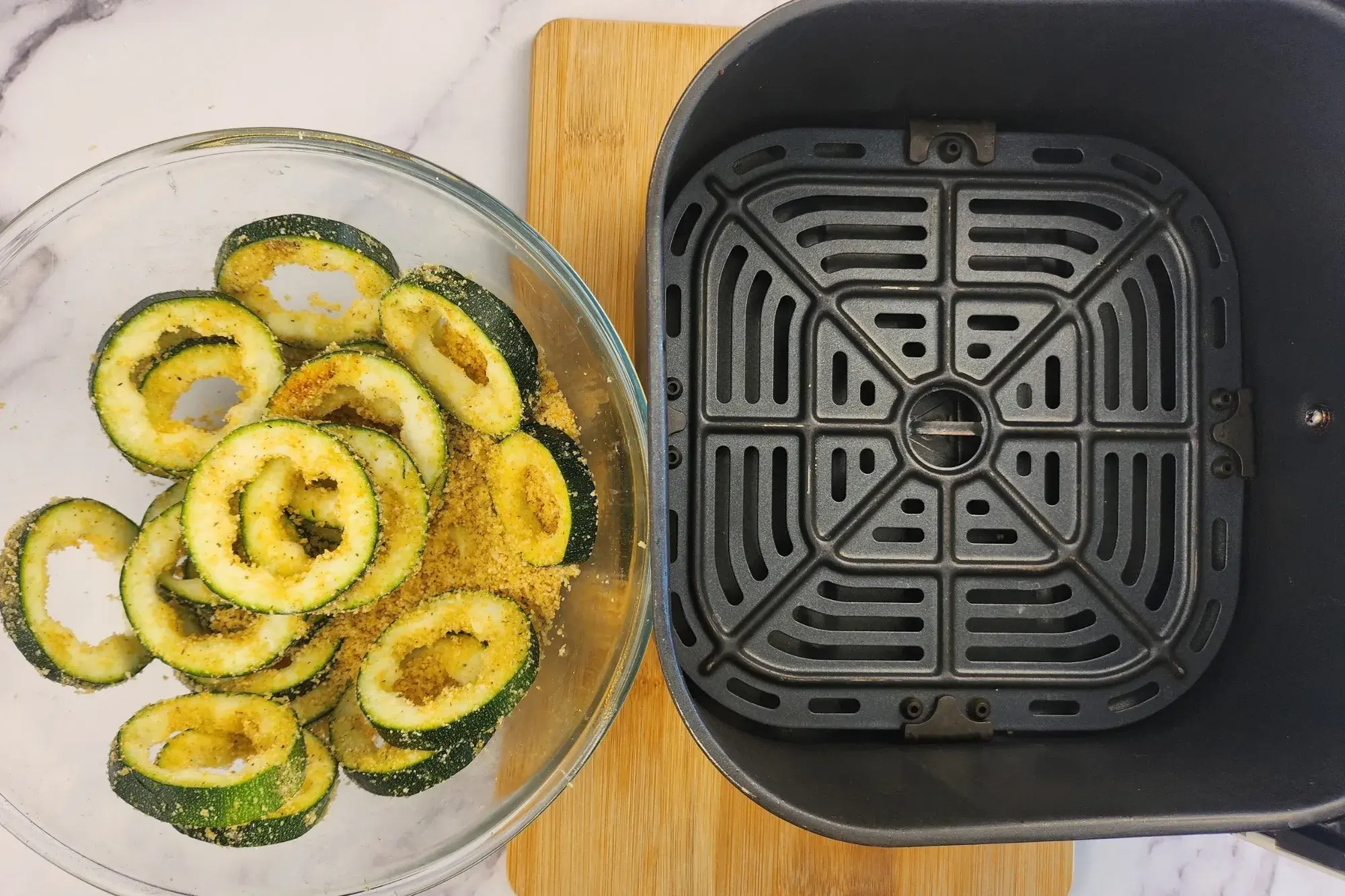 Zucchini rings in mixing bowl is next to basket of air fryer