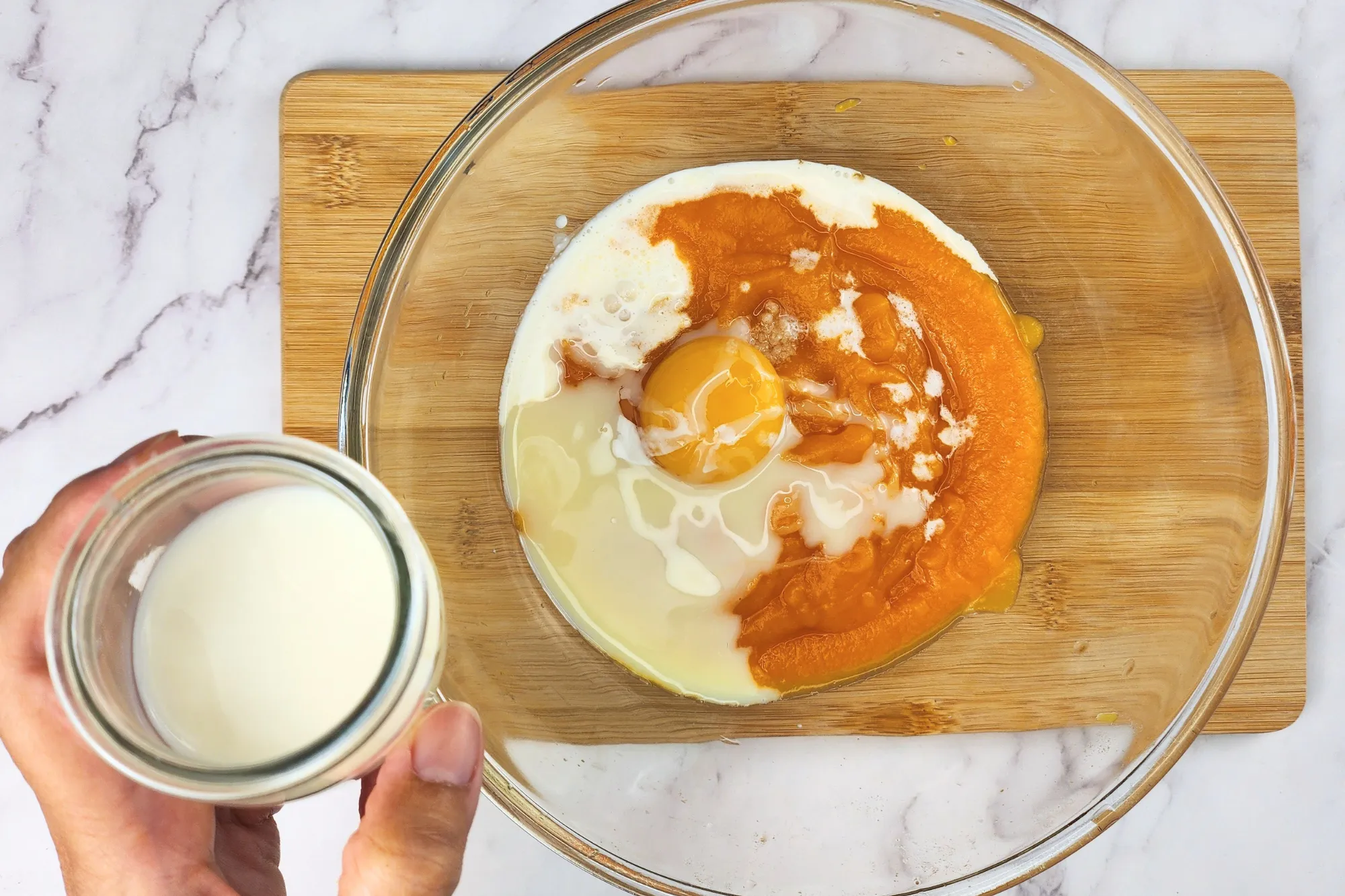 A hand is holding a jar of milk above a mixing bowl.