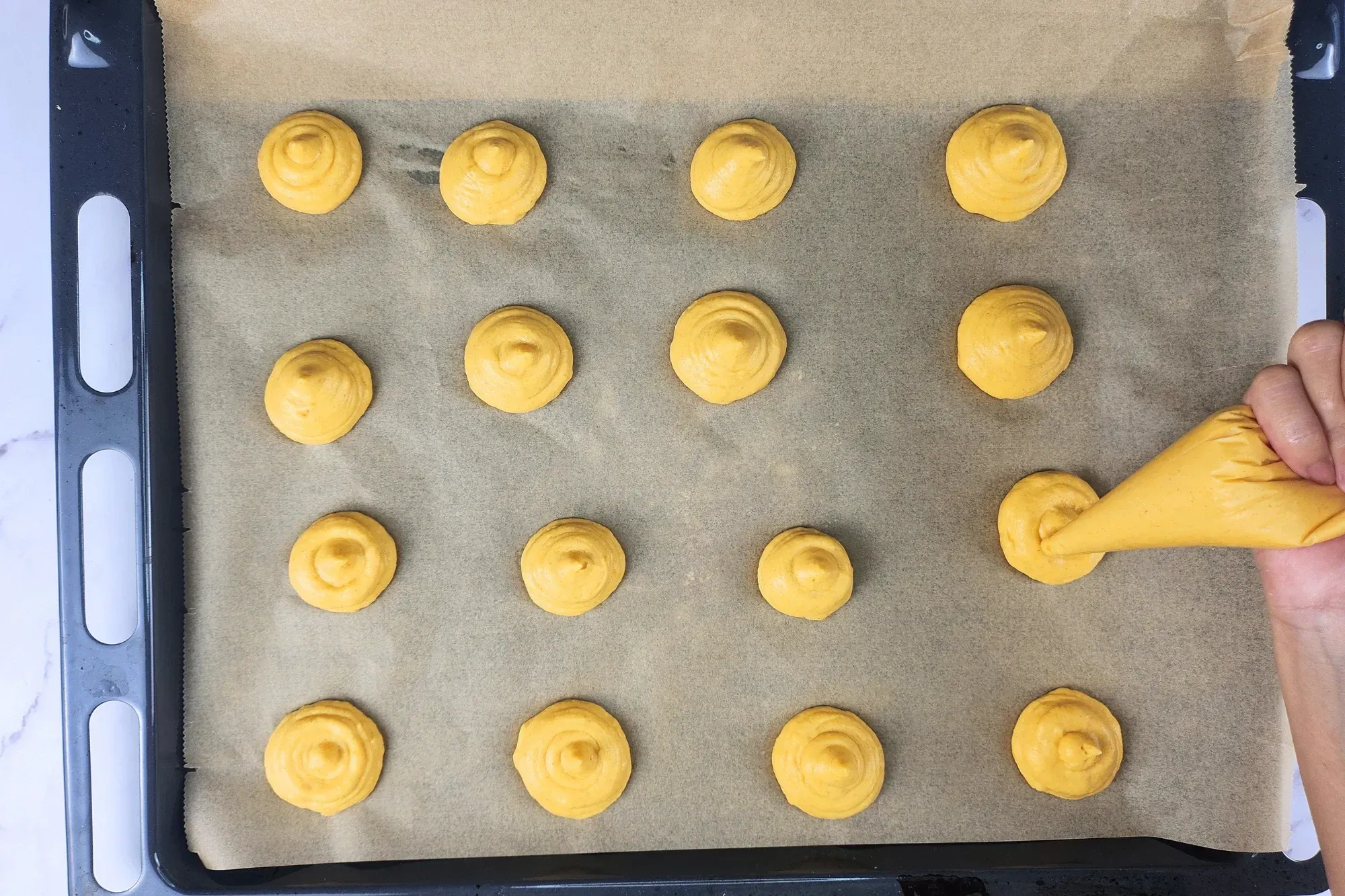 A hand is holding a piping bag with pumpkin puree mixed.