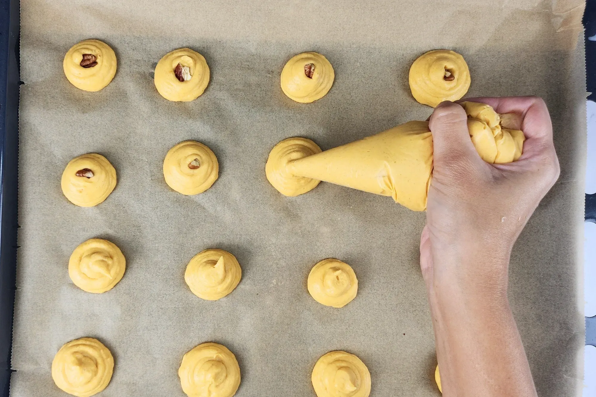 A hand is holding a pipping bag with pumpkin puree mixed
