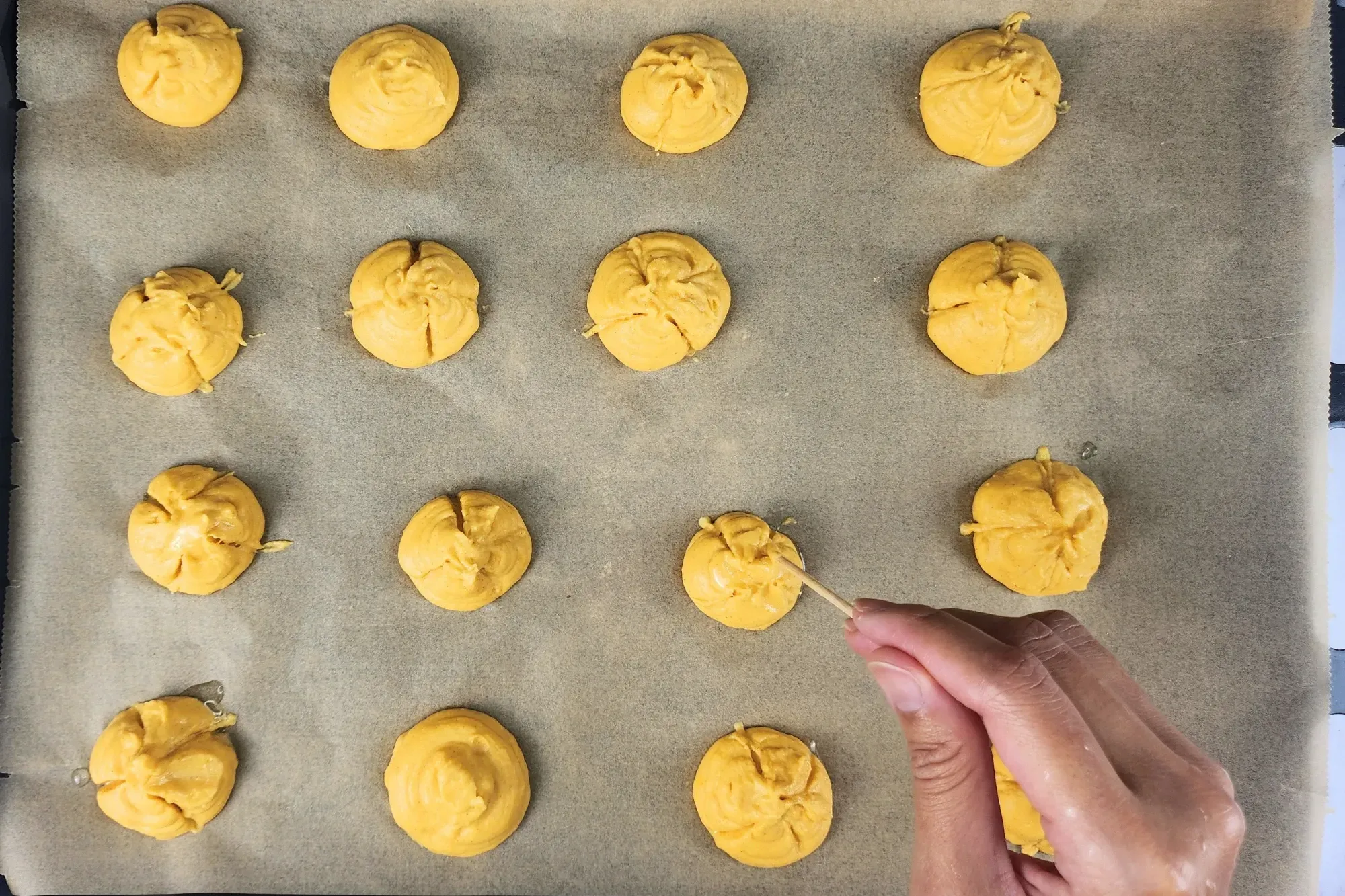 A hand is holding a screw above a pumpkin scoop on a baking paper