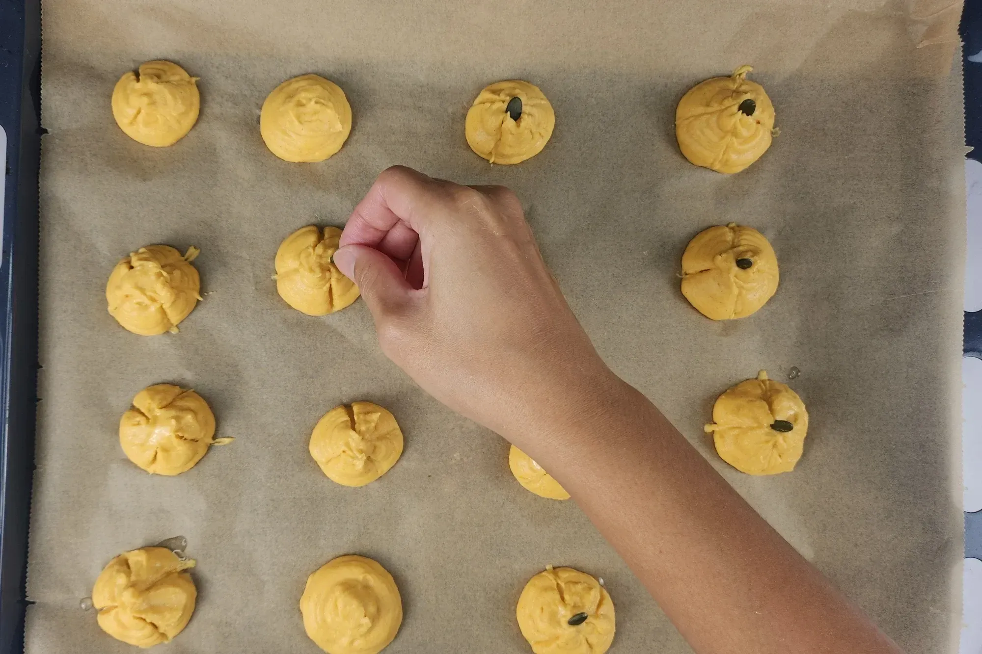 A hand is above pumpkin scoop on a baking paper