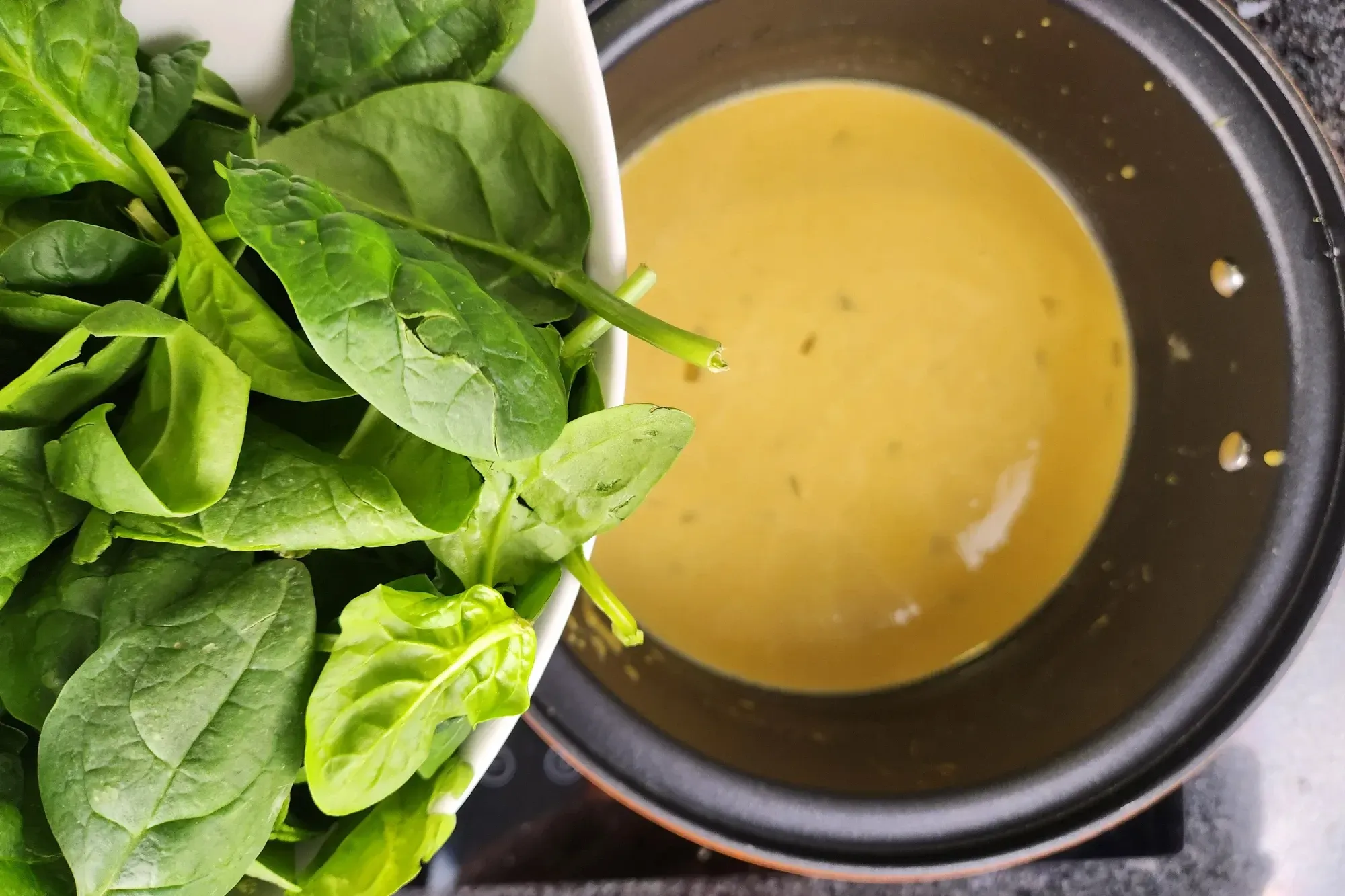 A bowl of baby spinach above a pot with yellow soup