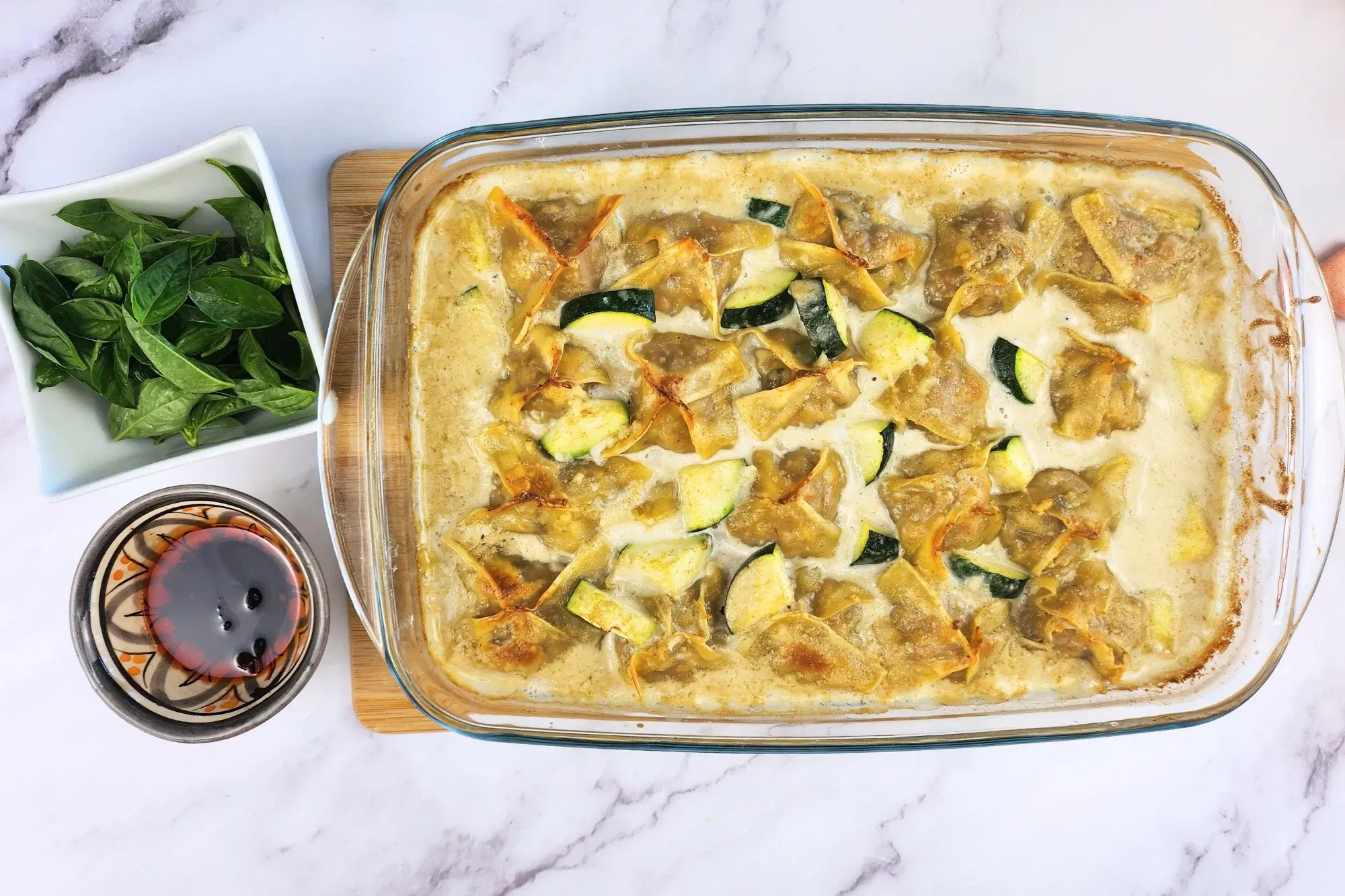 A bowl of basil leaves, a bowl of chili oil next to a tray of food.