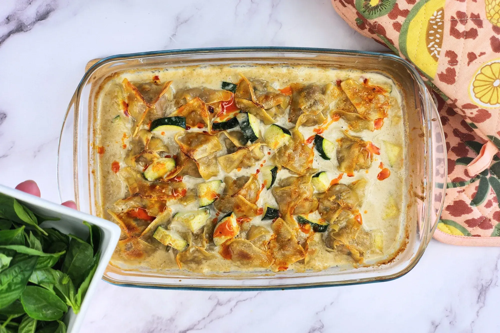 A bowl of basil leaves above a tray of food.