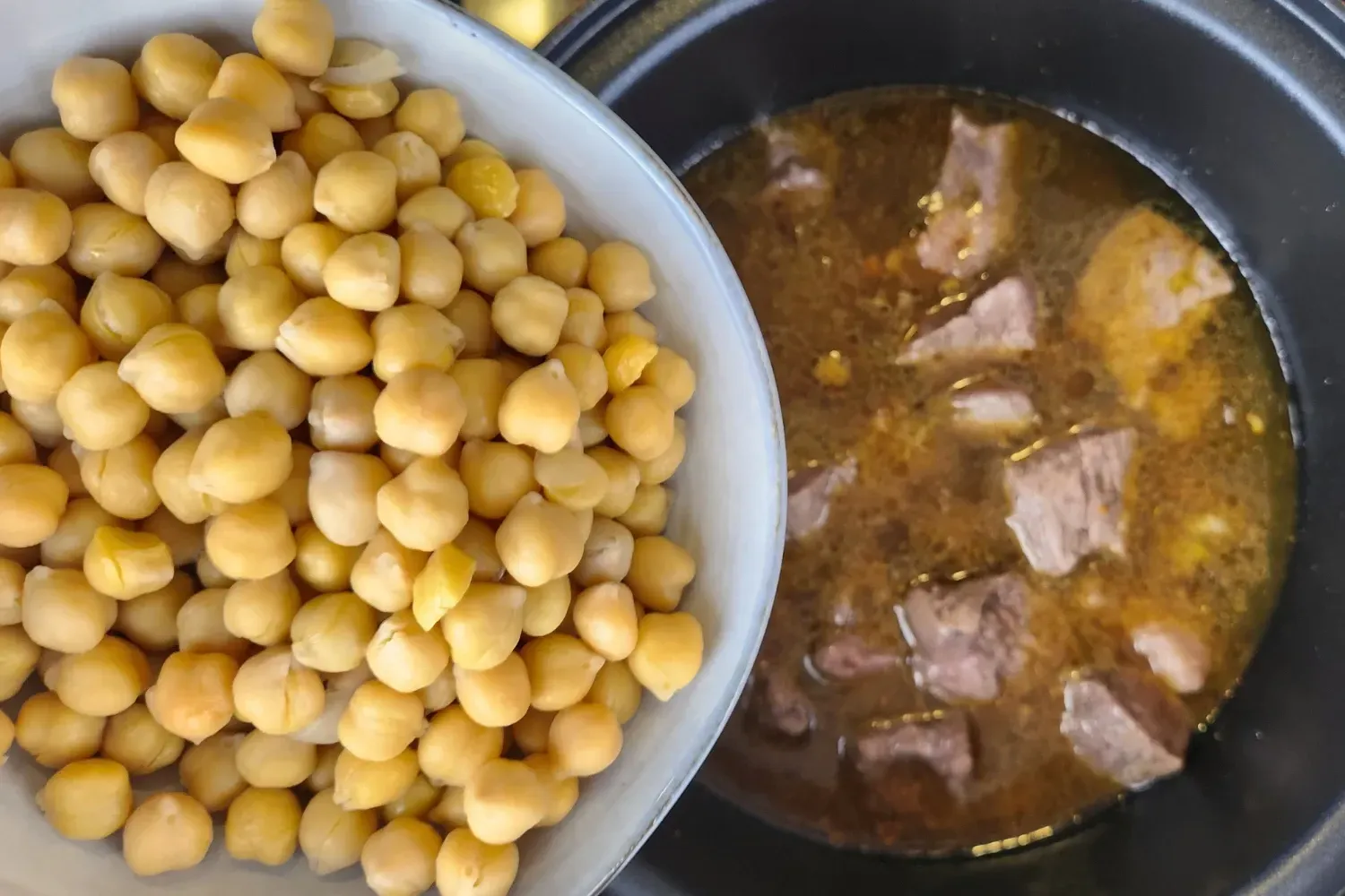 A bowl of chickpeas above a pot with meat.