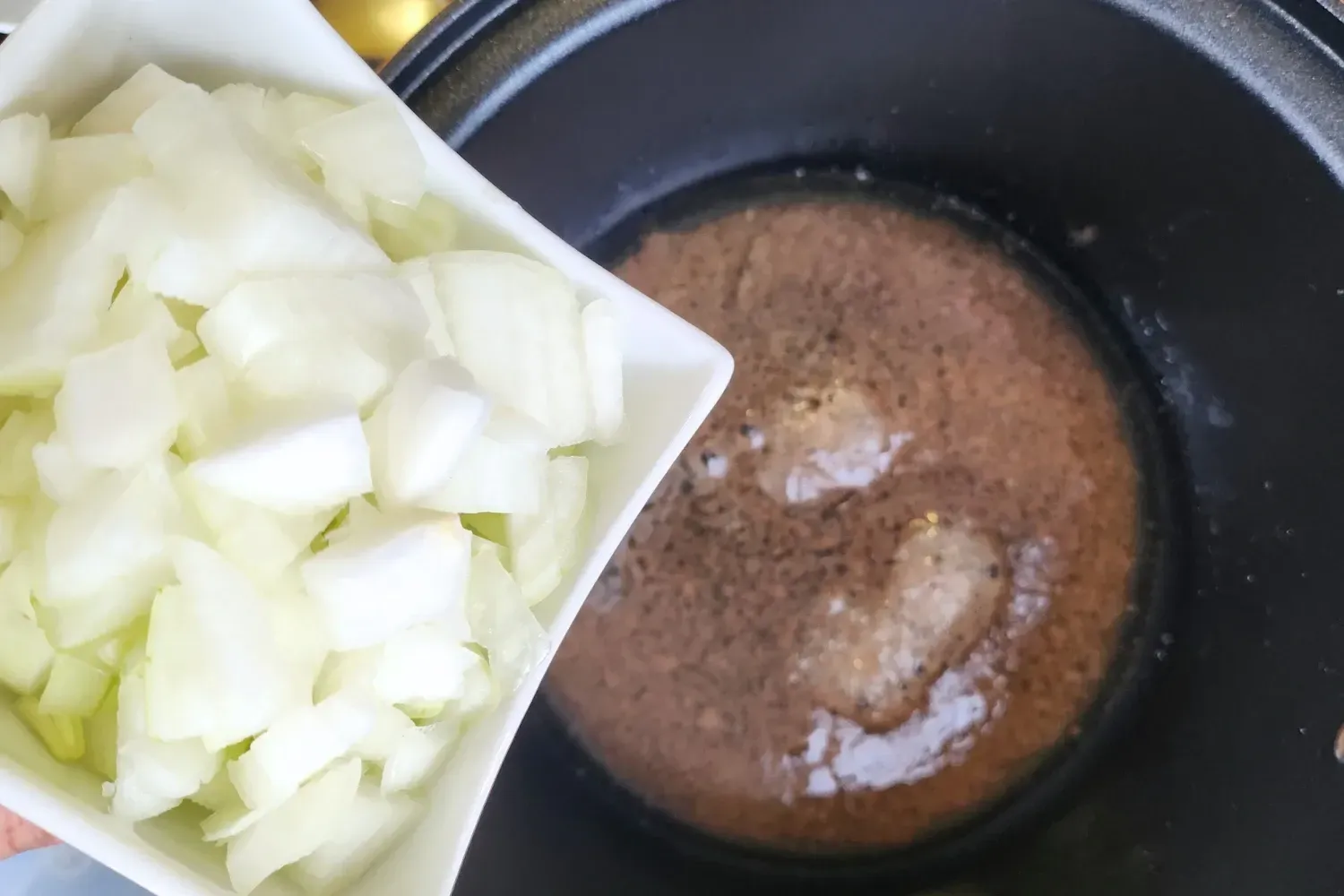 A bowl of chopped onions above a pot.
