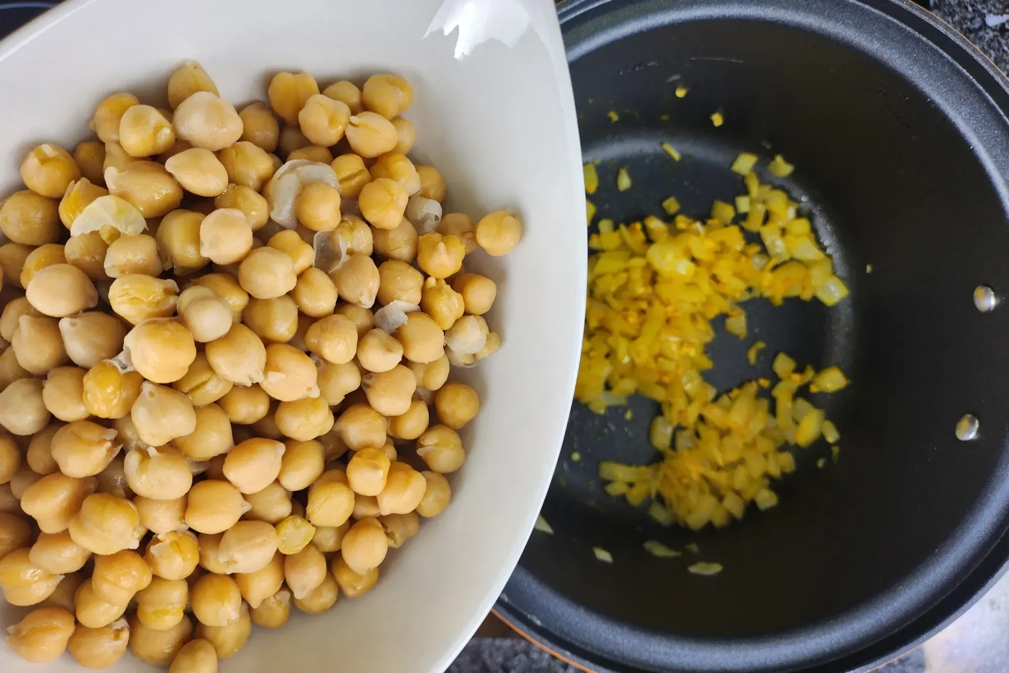 A bowl of cooked chicpea above a black pot with cooked onion