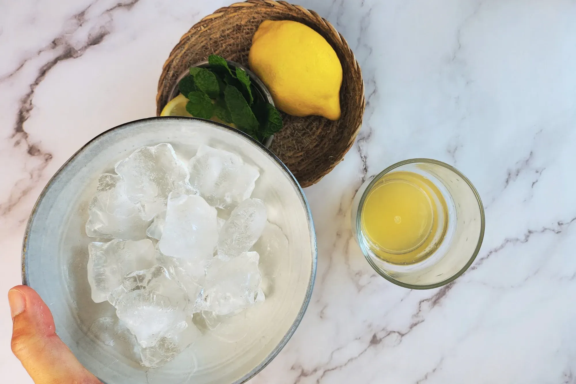 A bowl of ice next to lemon and a glass.