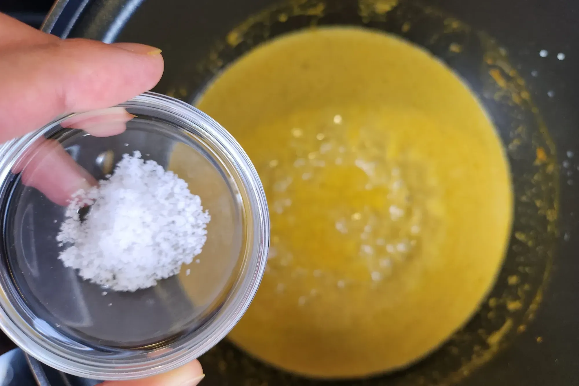 A bowl of salt  is being holding above the curry pot.