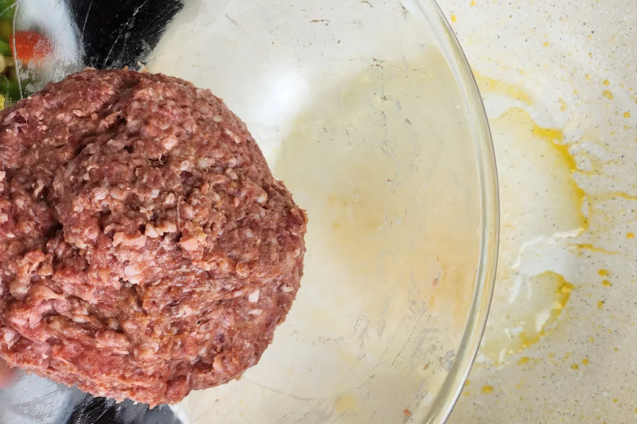 A bowl of seasoned ground beef above an used wok.