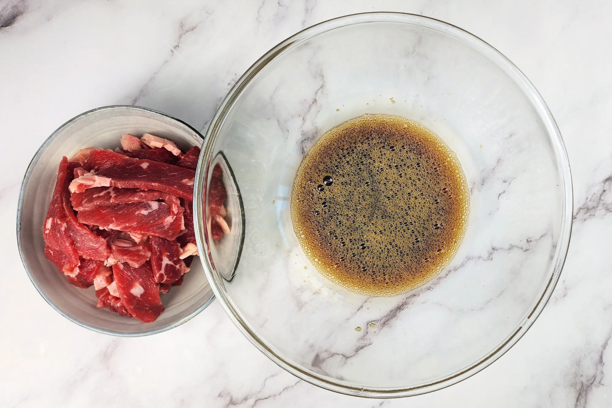 A bowl of sliced beef is next to a mixing bowl with sauce.
