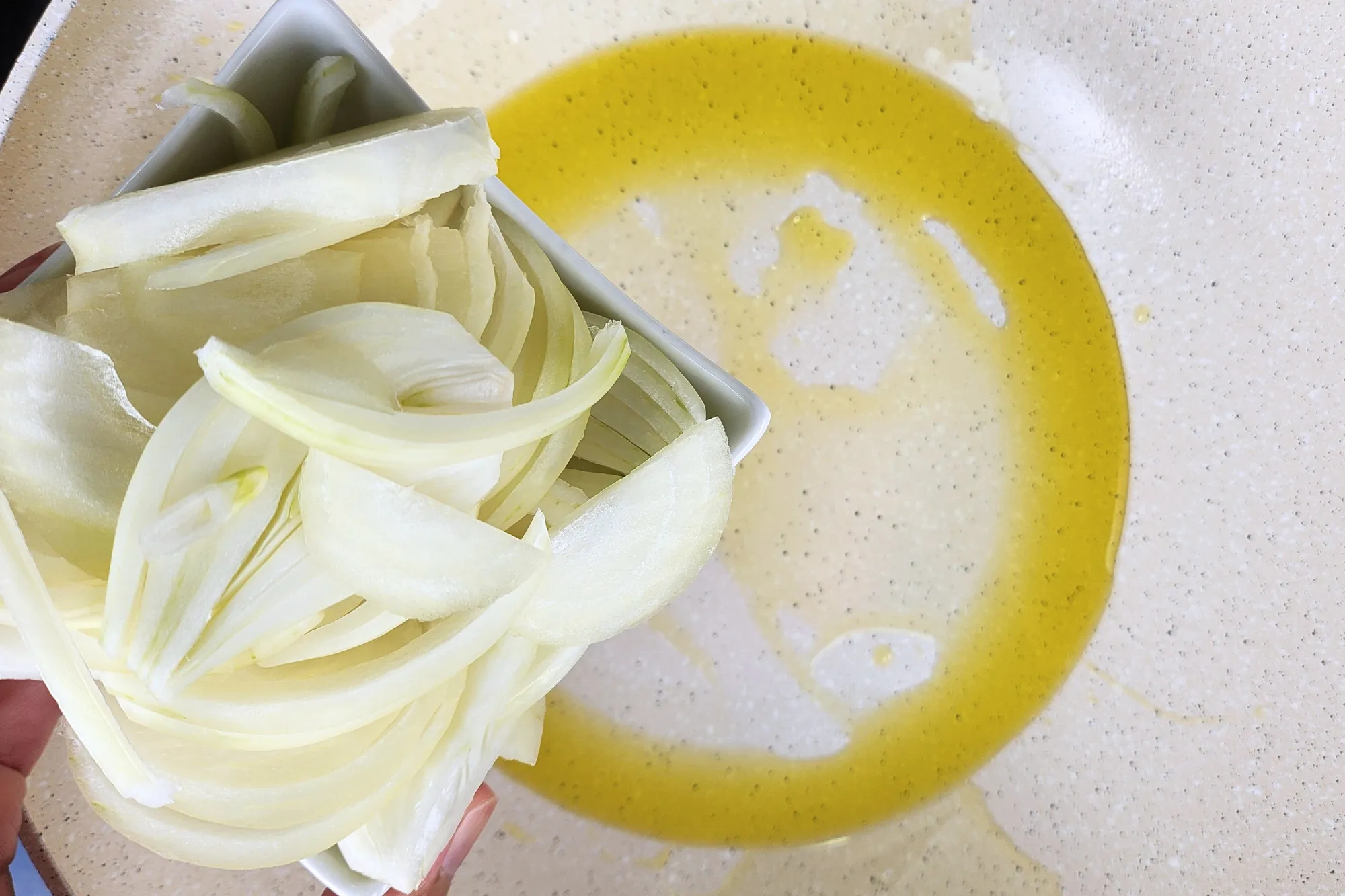A bowl of sliced onion above hot oil in a wok.