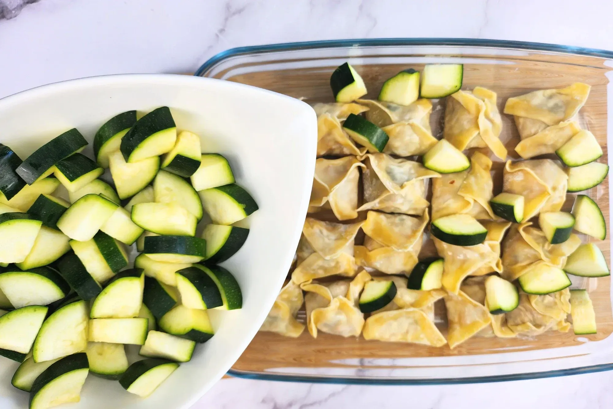 A bowl of zucchini is above a tray of dumplings.
