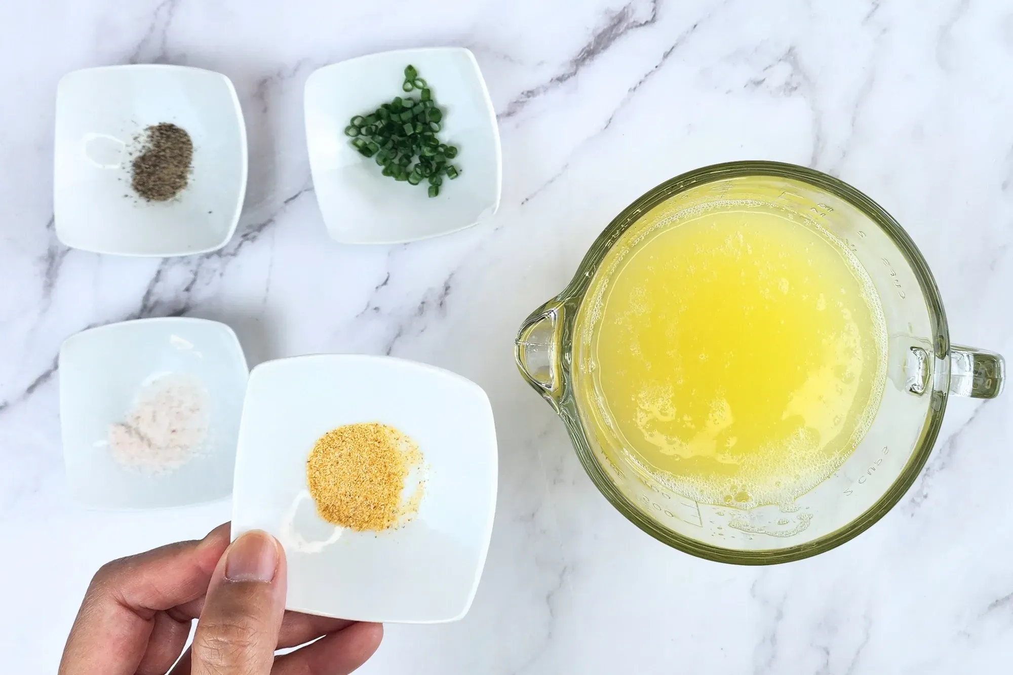A hand holding a bowl of garlic powder above the egg white and others ingredients