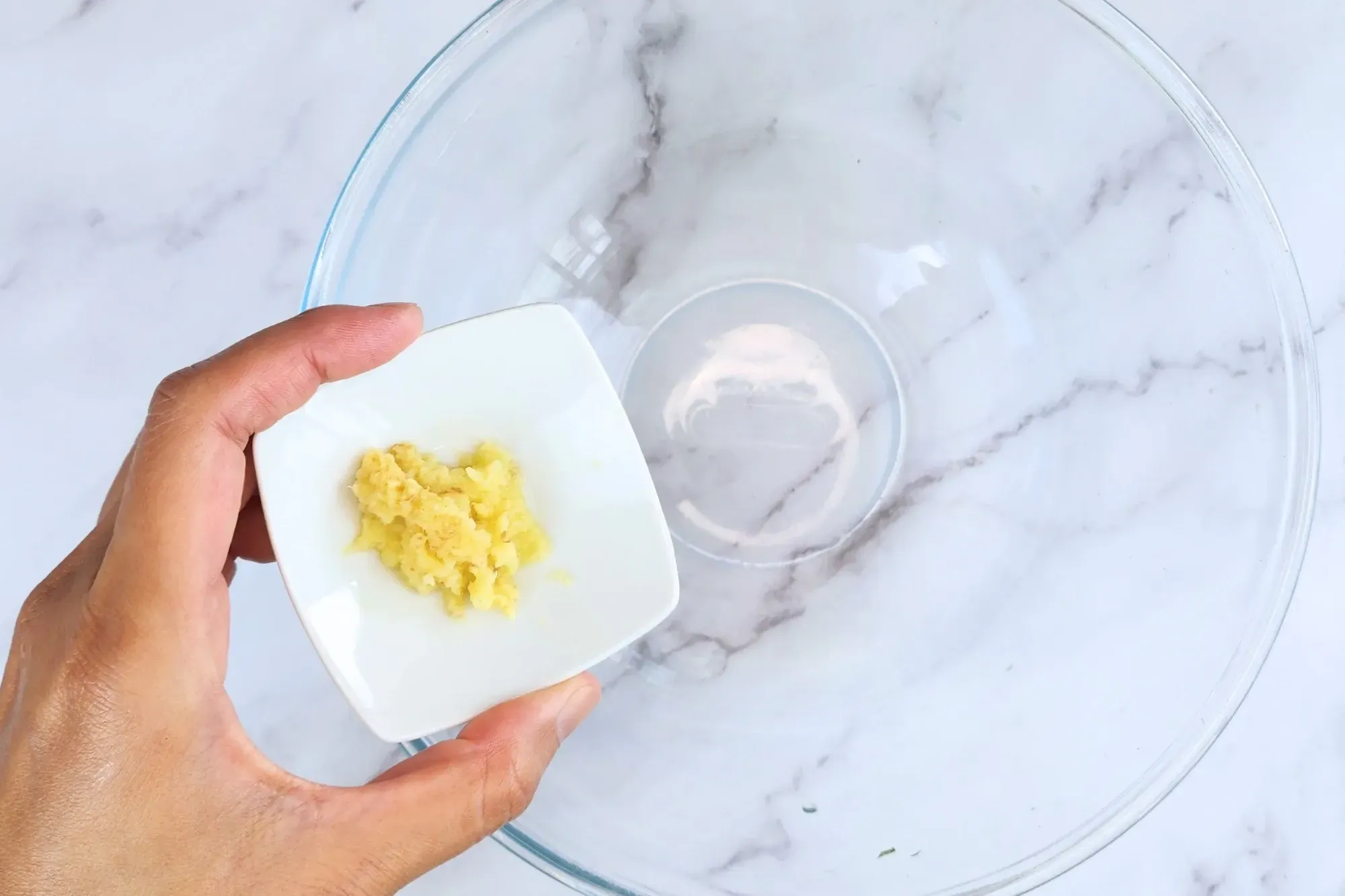 A hand holding a bowl of grated ginger above the dressing bowl