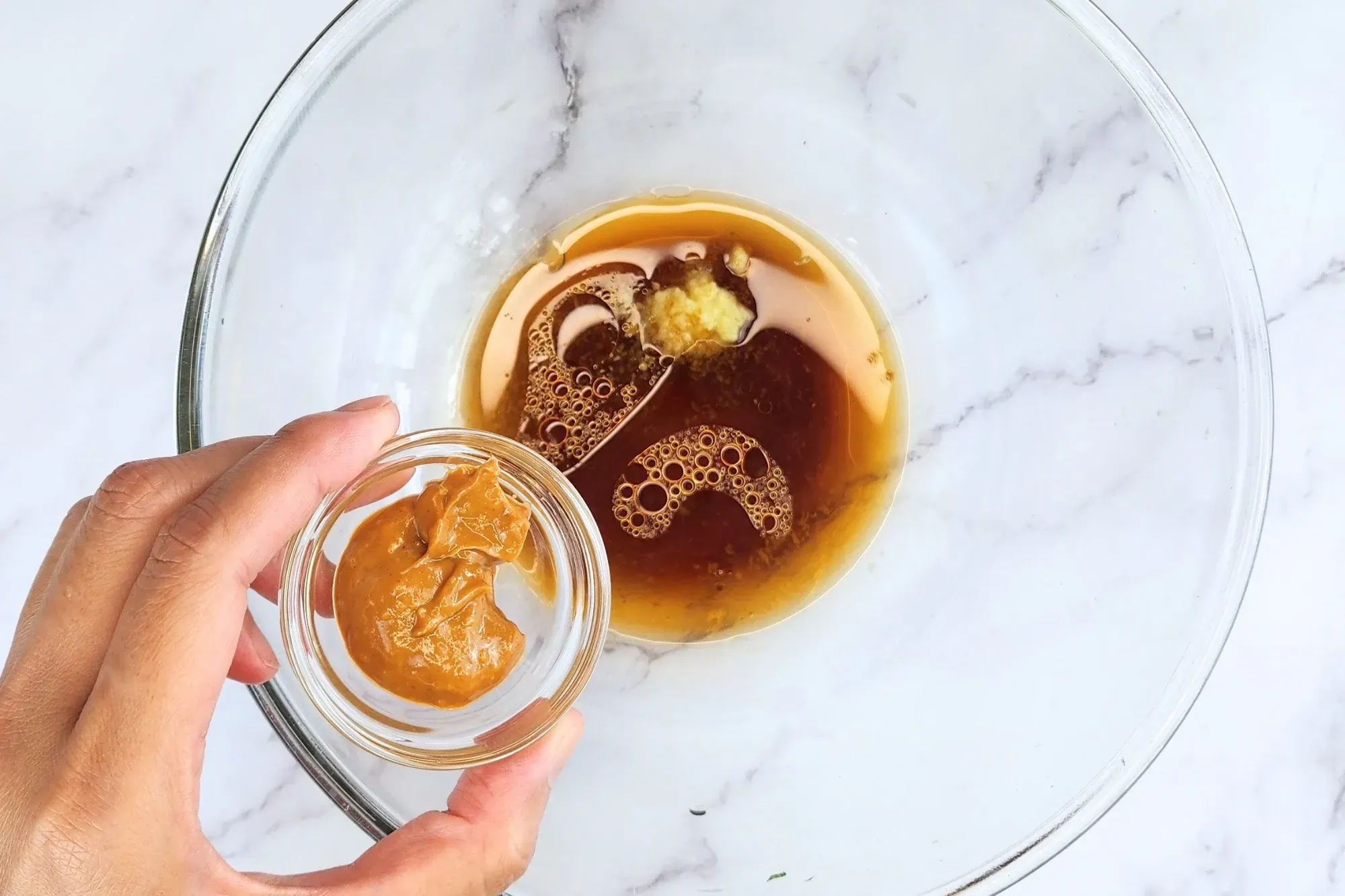 A hand holding a bowl of peanut butter above the dressing bowl