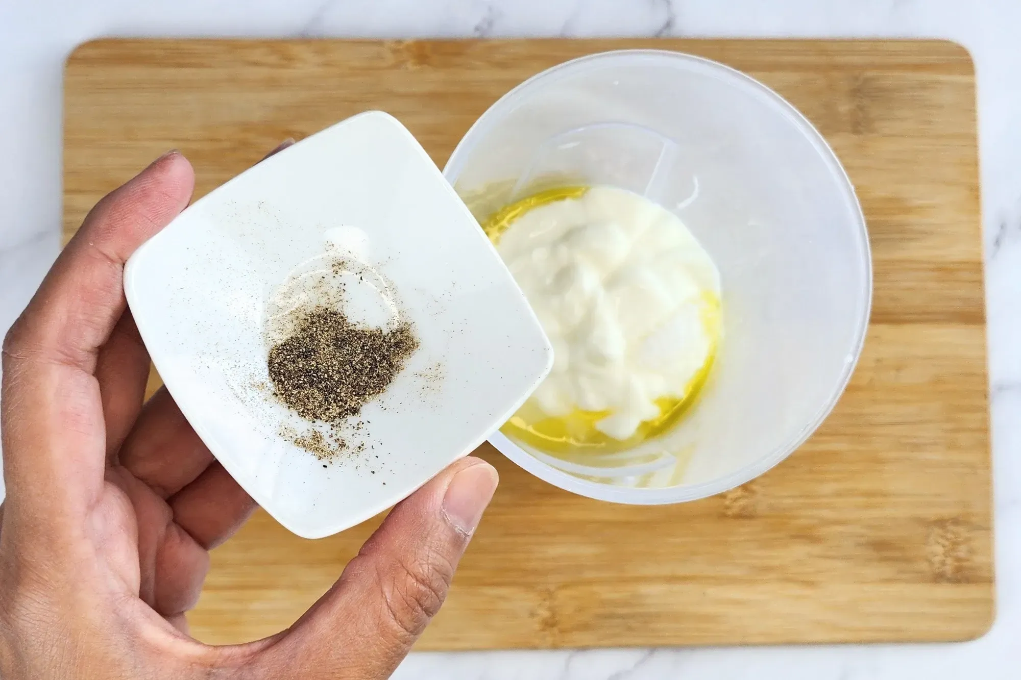 A hand is hold a bowl of black pepper above a jar of cooked center of zucchini. 