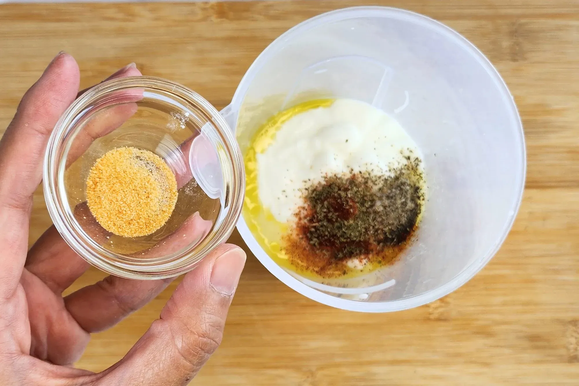 A hand is hold a bowl of garlic powder above a jar of cooked center of zucchini