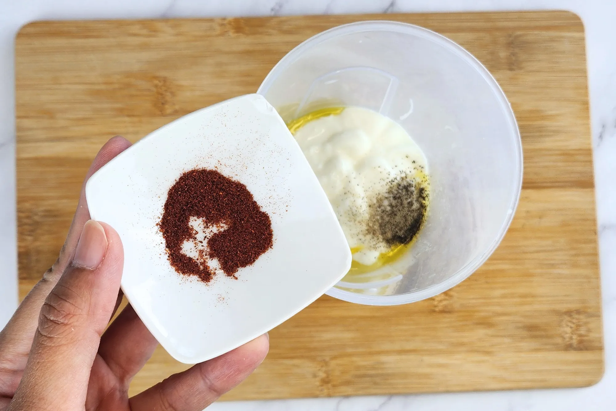 A hand is hold a bowl of paprika above a jar of cooked center of zucchini