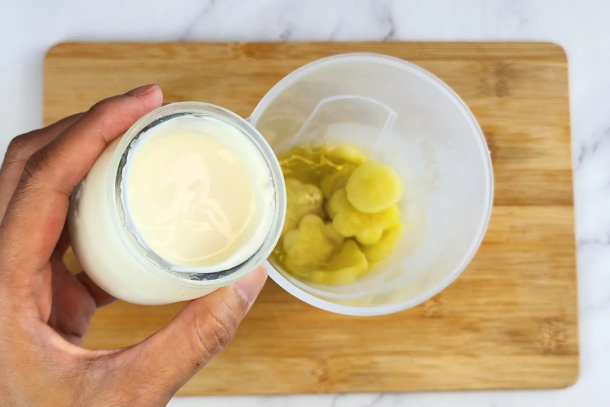 A hand is hold a jar of yogurt above a jar of cooked center of zucchini