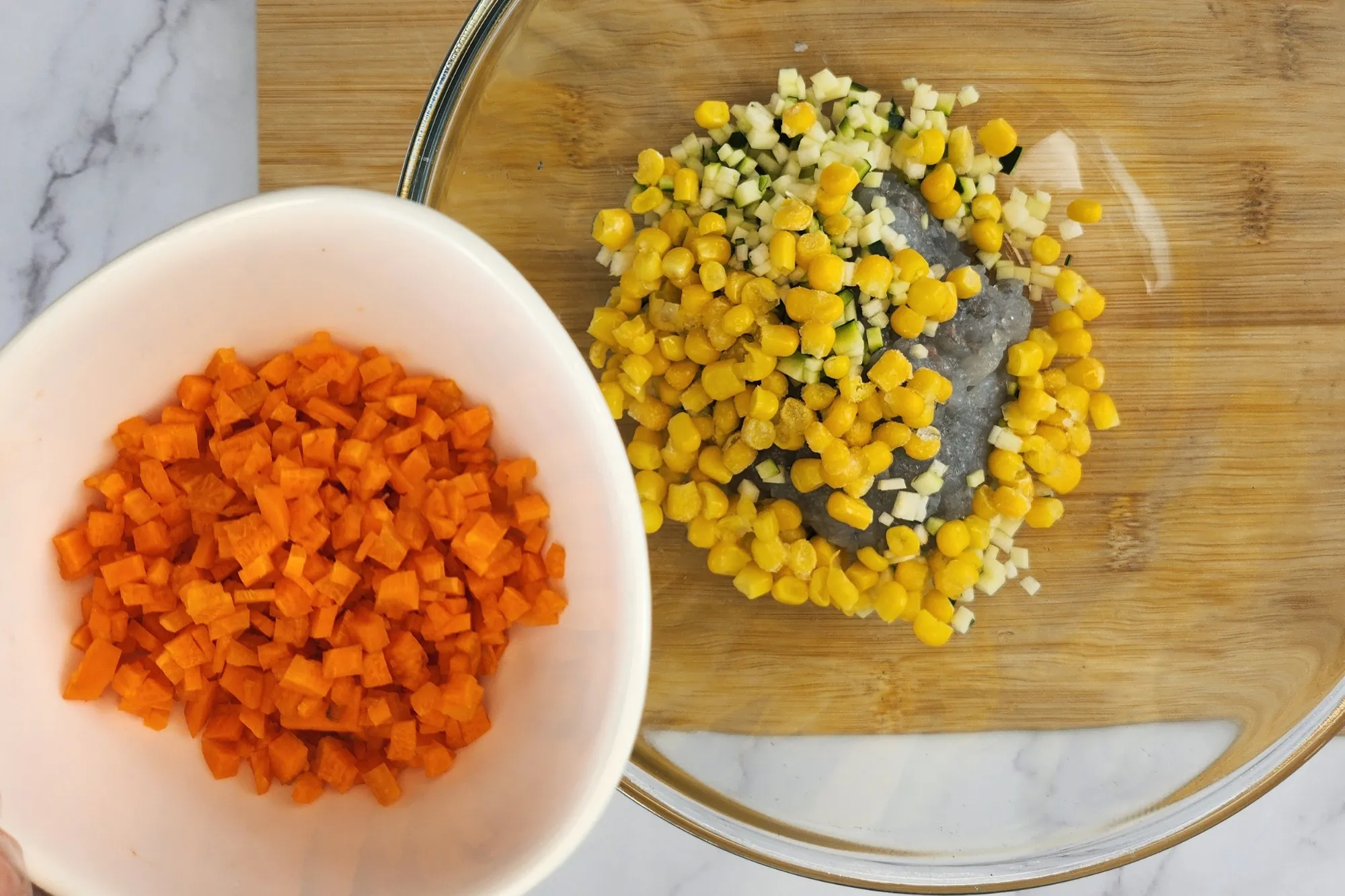 A hand is holding a bowl of chopped carrrots above a mixing bowl
