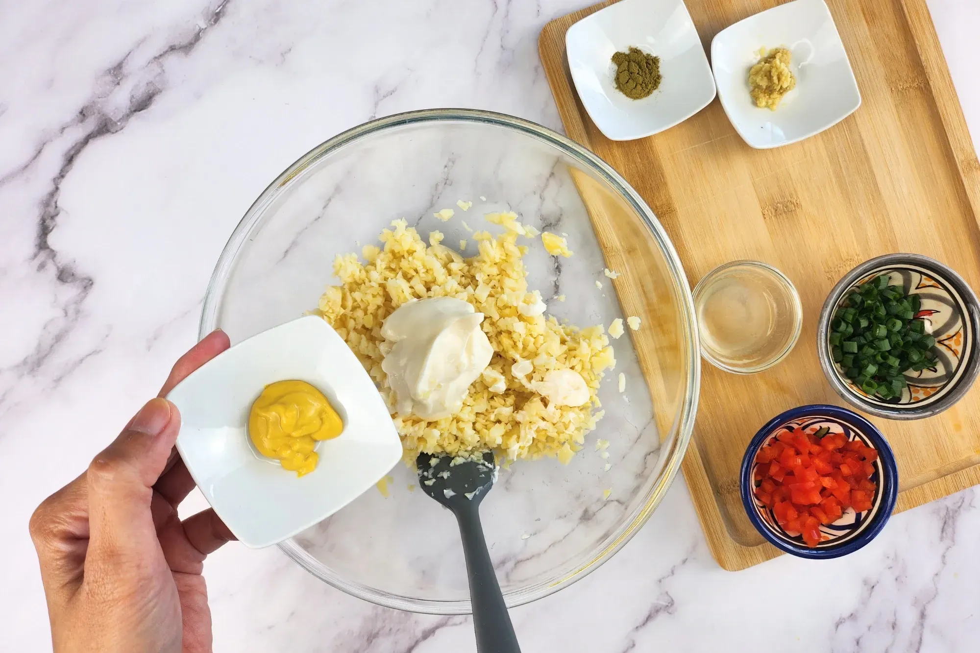 A hand is holding a bowl of dijon mustard above the mixing bowl.