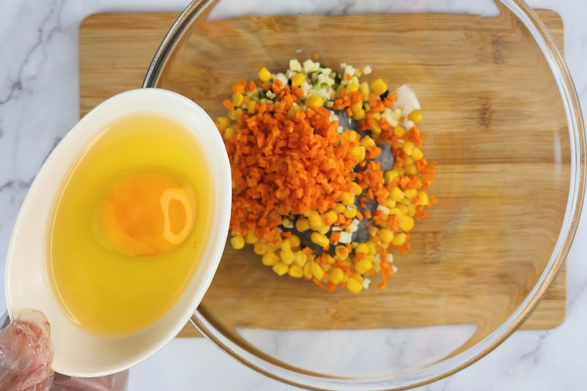 A hand is holding a bowl of egg above a mixing bowl